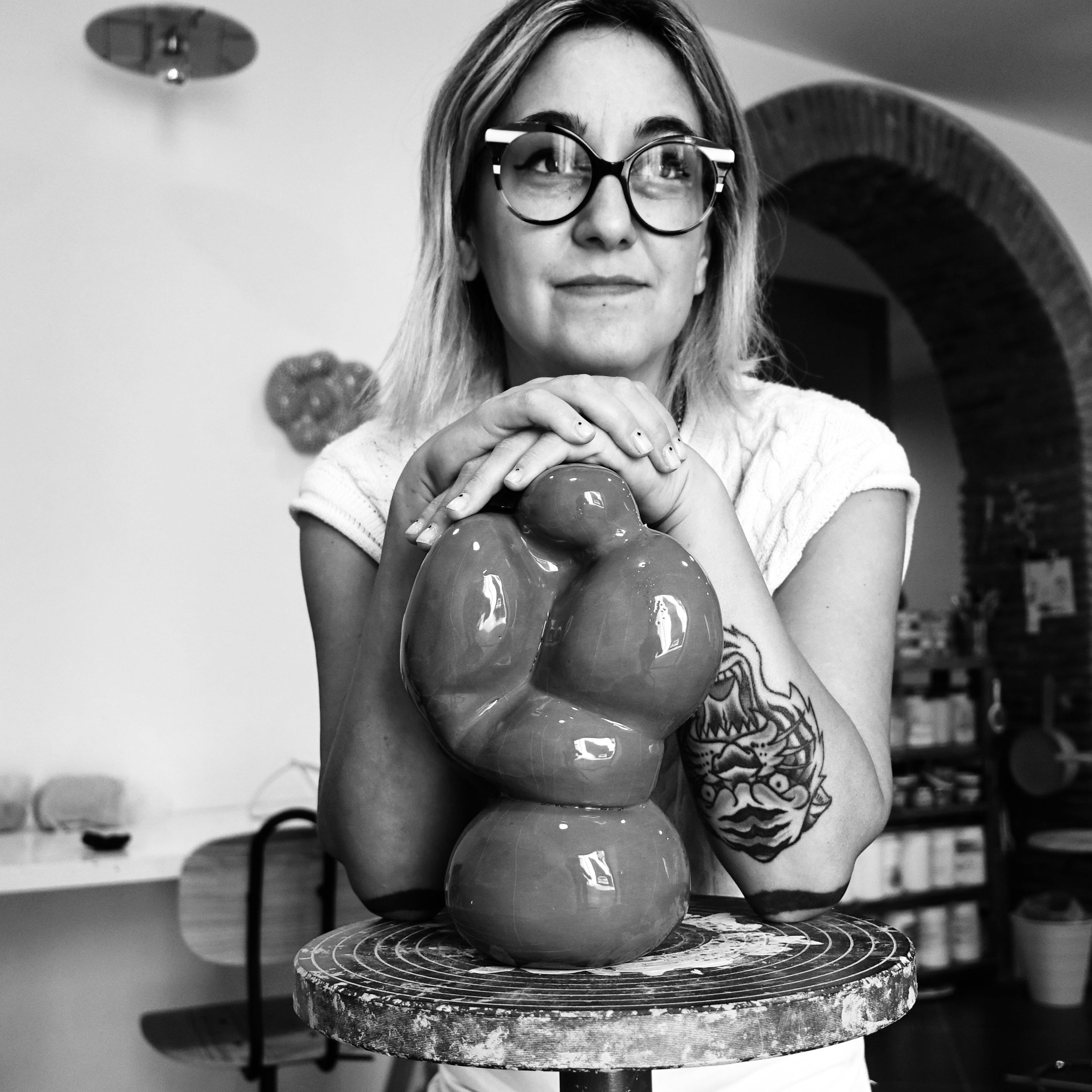Die Keramikkünstlerin Alie de Ferraro steht in ihrem Atelier und stützt sich auf einer Keramikskulptur auf