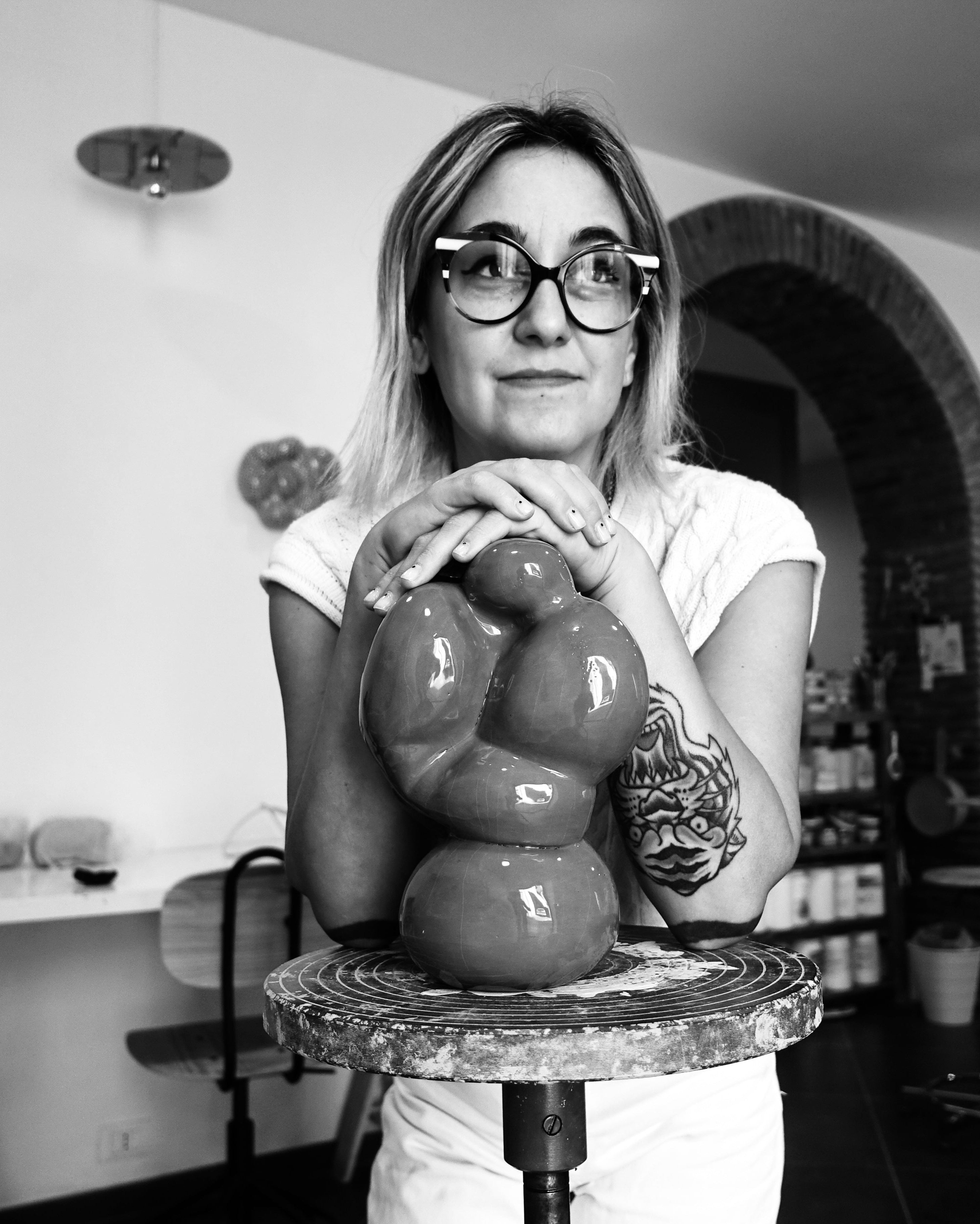 Die Keramikkünstlerin Alie de Ferraro steht in ihrem Atelier und stützt sich auf einer Keramikskulptur auf