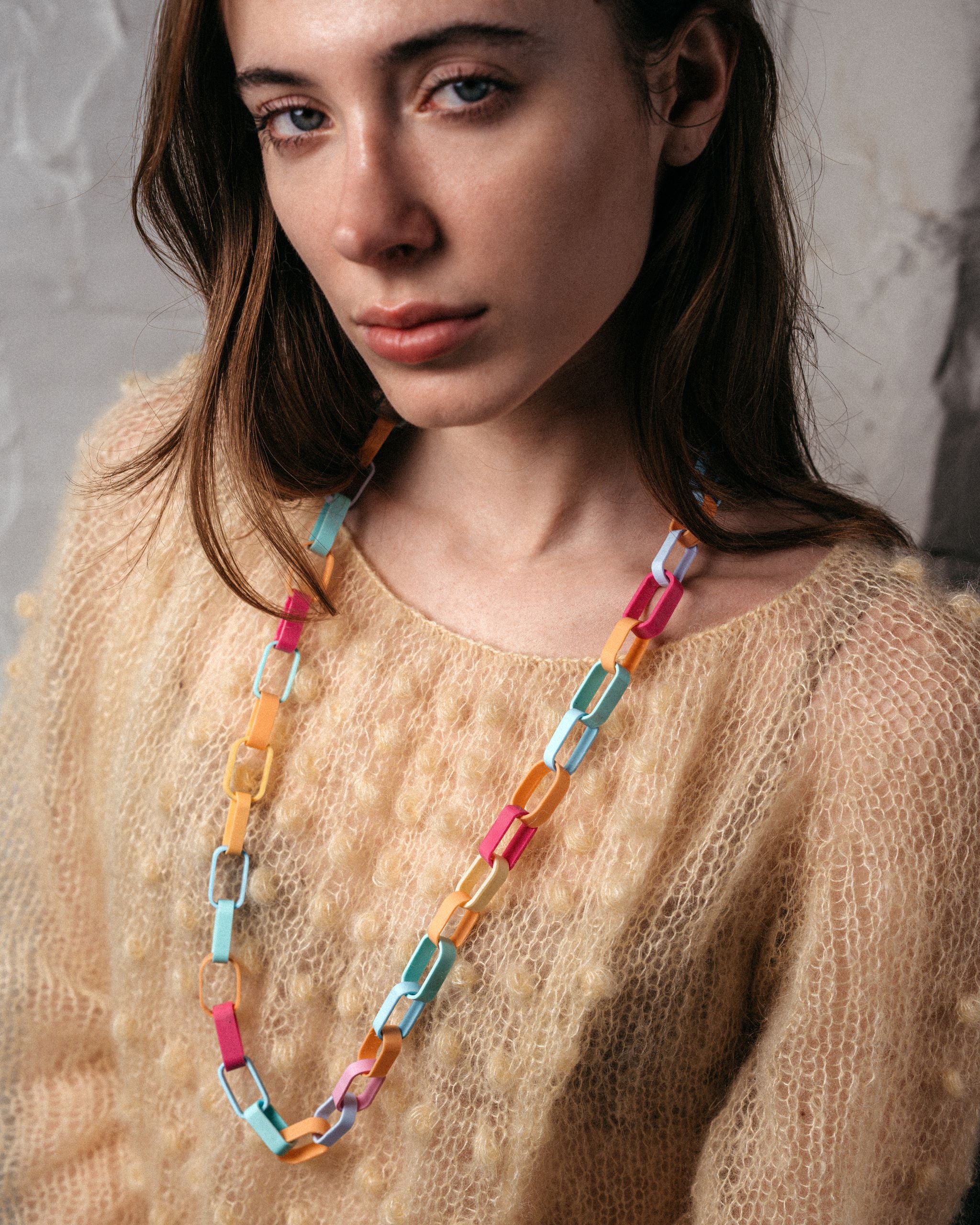 Ein Model trägt eine Gliederkette der Schmuckdesignerin Carla Movia, deren große Glieder in pastelligen, aber kräftigen Farben aus recyclten Hülsen von Textmarkern bestehen.