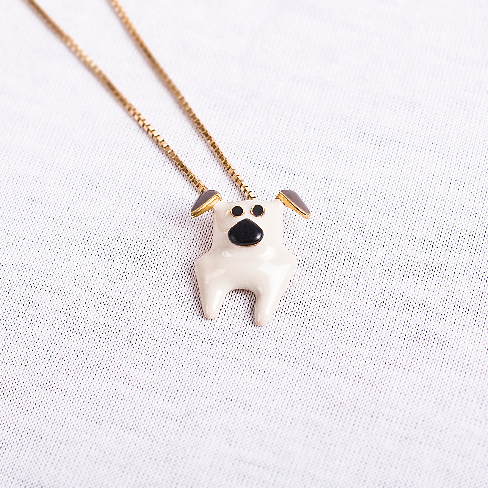 Eine schmale goldene Halskette mit einem Anhänger in Form eines weissen Mops mit grauen Ohren und schwarzer Schnauze der italienischen Schmuckdesignerin Chiara Bello von chic pig.