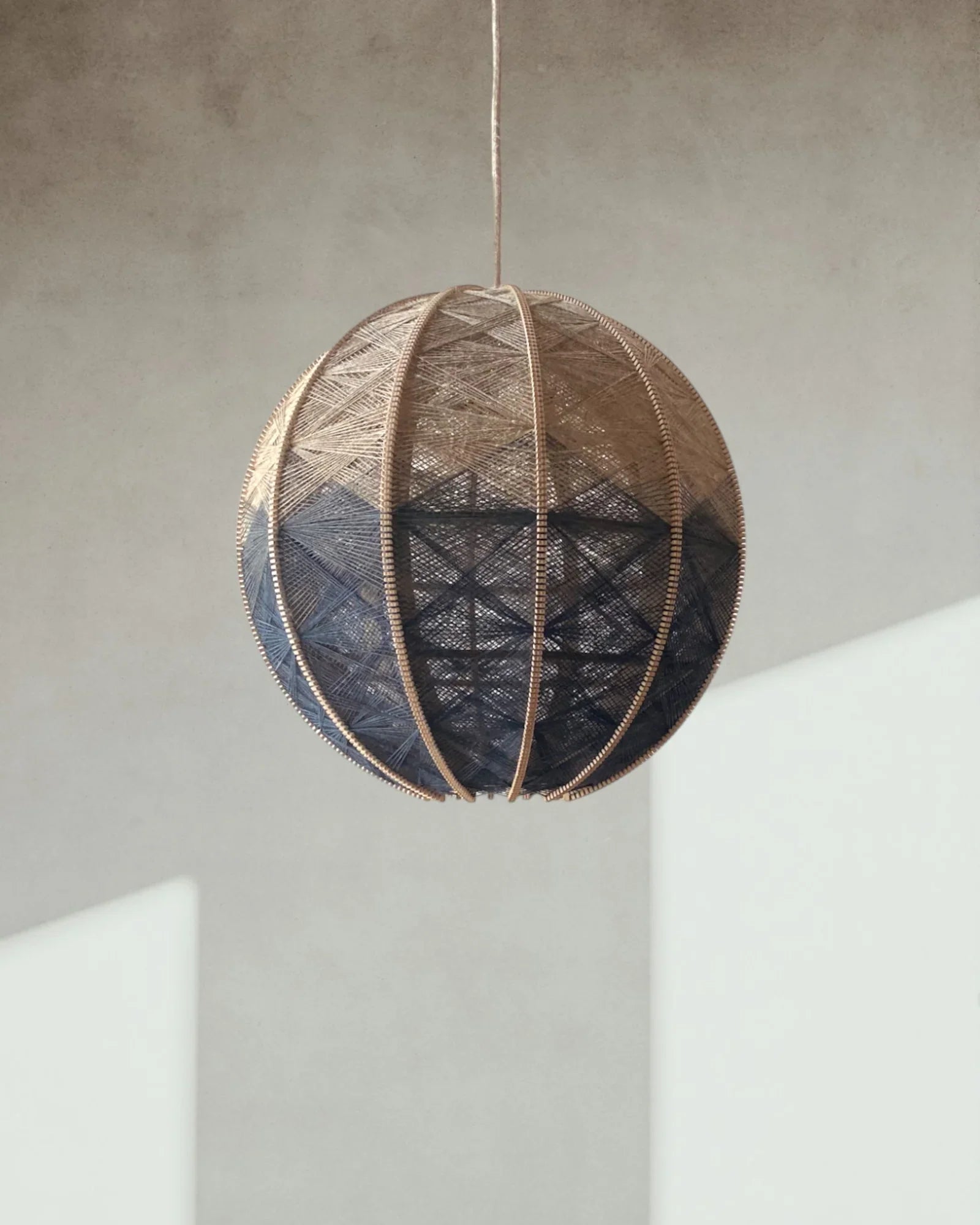 eine runde Hängeleuchte aus Birkenholz umwebt mit Leinengarn in Anthrazit und Beige hängt vor einer Wand