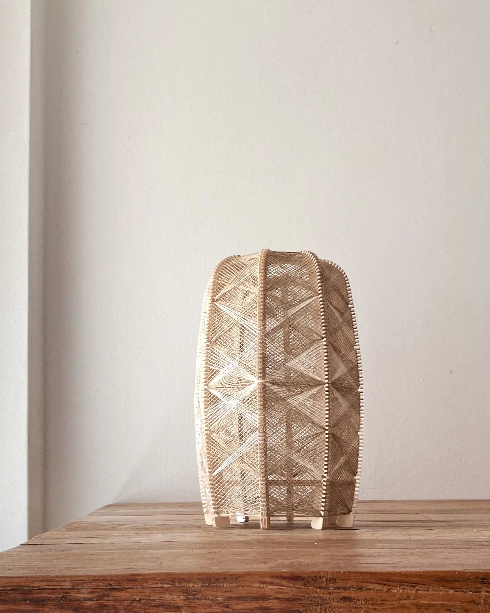 eine zylindrisch Tischleuchte aus Birkenholz und gewebtem Leinengarn in Beige steht auf einem Holztisch