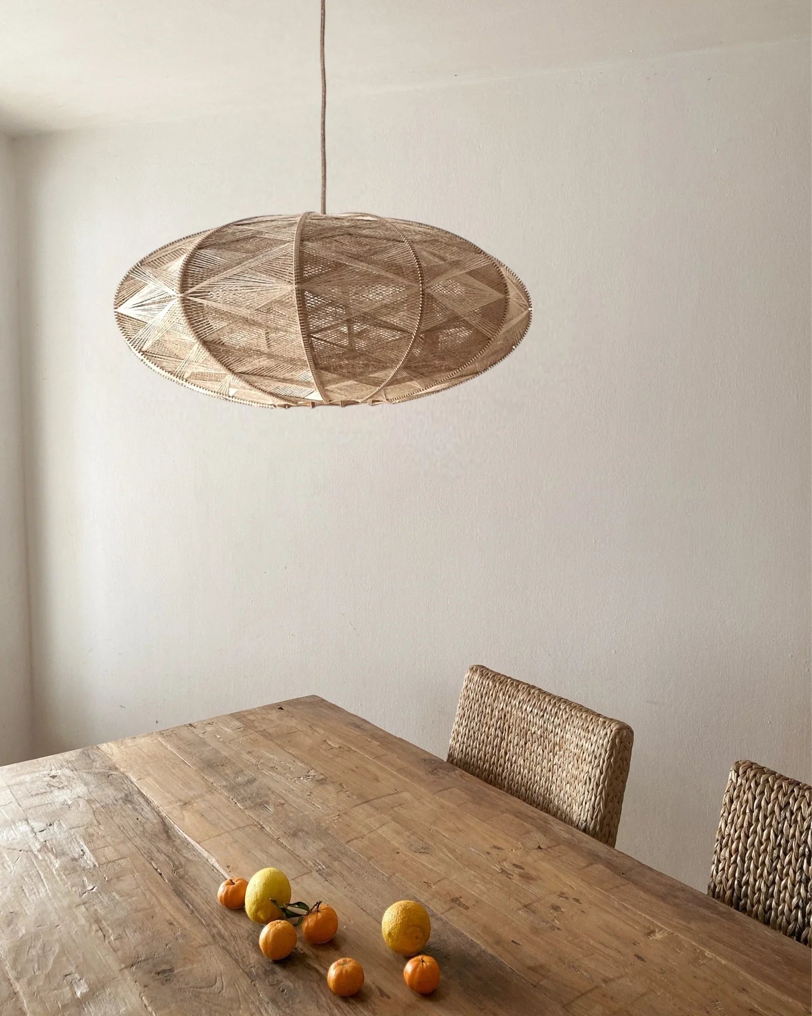 eine elliptische Hängeleuchte aus Birkenholz umwebt mit beigem Leinengarn hängt über einem Esstisch mit Zitrusfrüchten