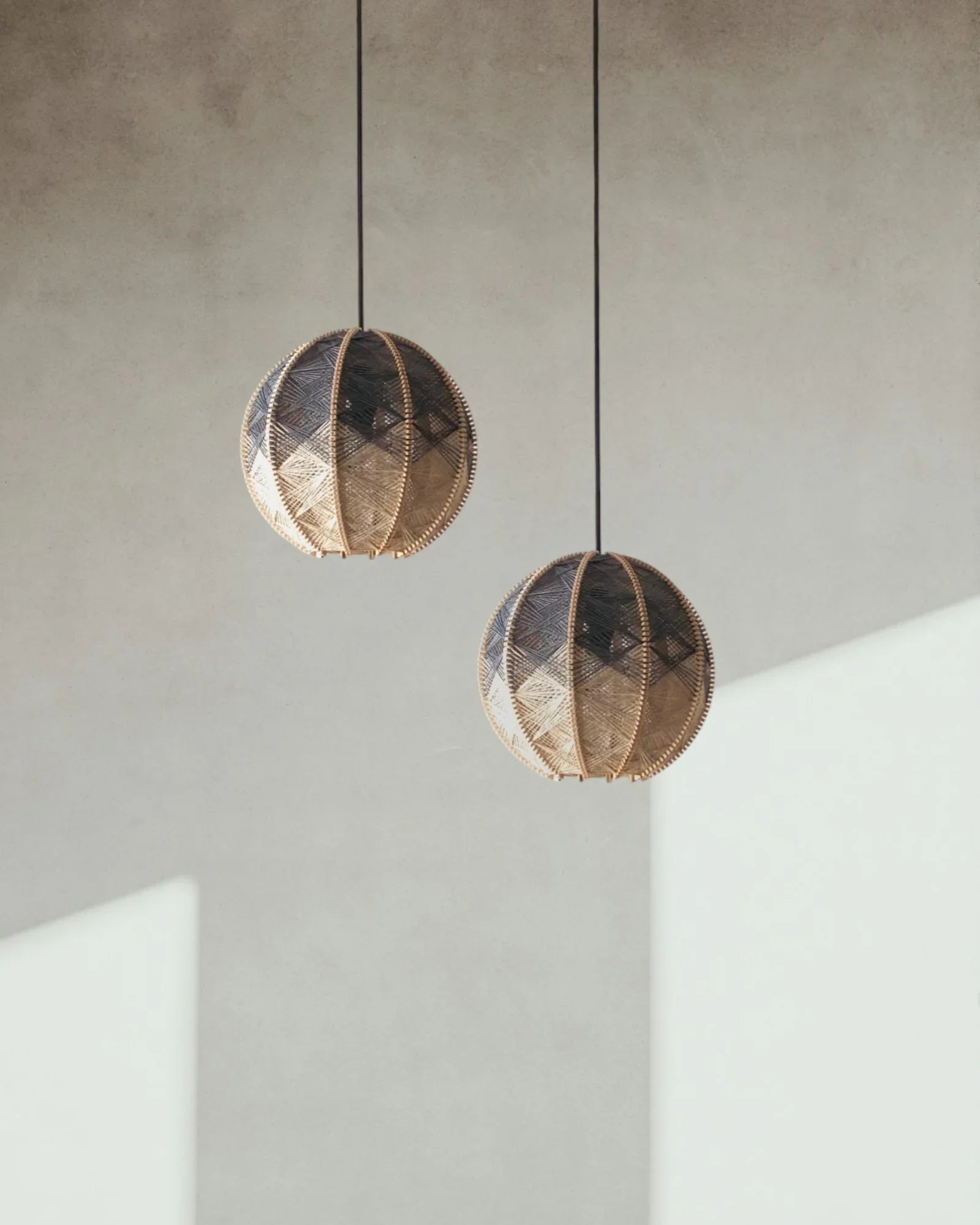 zwei runde Hängeleuchten aus Birkenholz umwebt mit Leinengarn in Beige und Anthrazit hängen versetzt vor einer Wand
