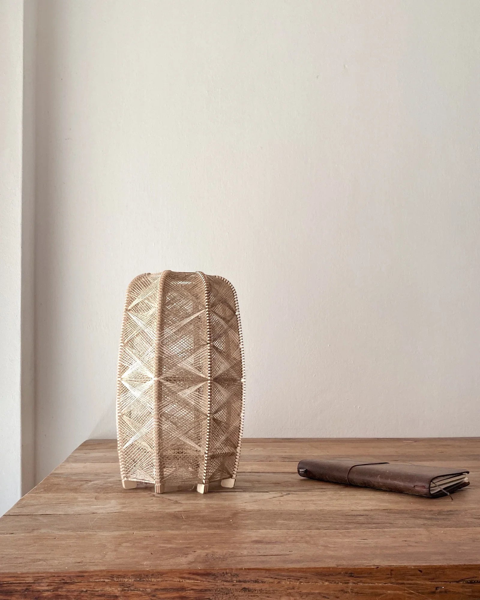 eine zylindrisch Tischleuchte aus Birkenholz und gewebtem Leinengarn in Beige steht auf einem Holztisch