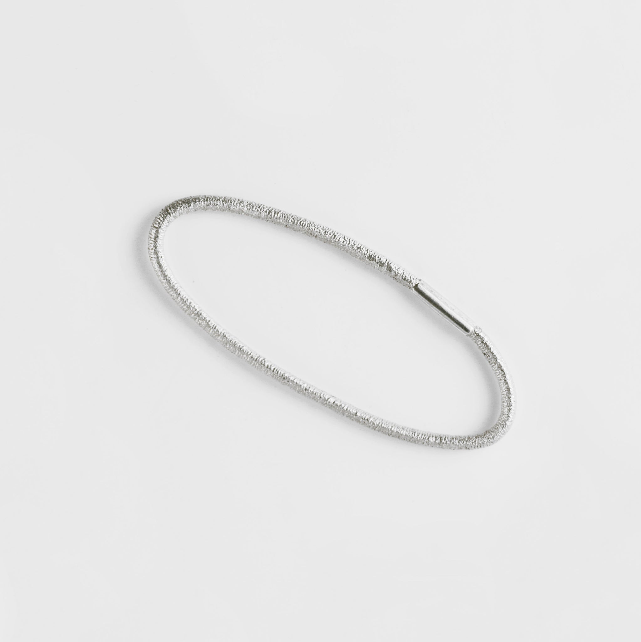 Ein Drei-Finger-Ring, der aussieht, wie ein dünnes Haargummi, das man über drei Finger spannt - hergestellt von Goldschmiedin Annie Sibert.