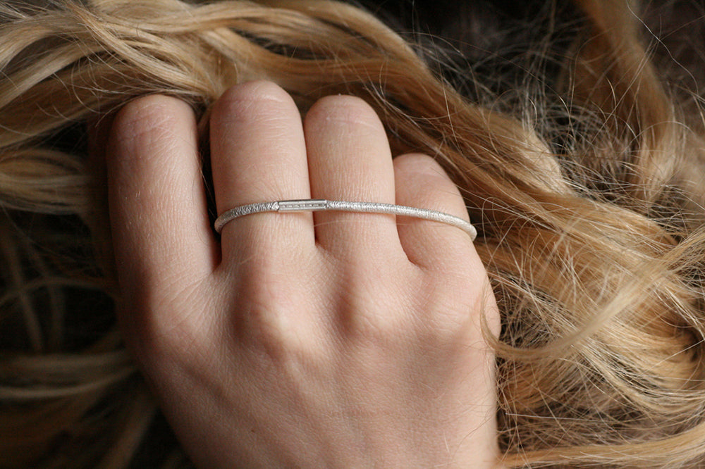 Ein Drei-Finger-Ring, der aussieht, wie ein dünnes Haargummi, das man über drei Finger spannt - hergestellt von Goldschmiedin Annie Sibert.