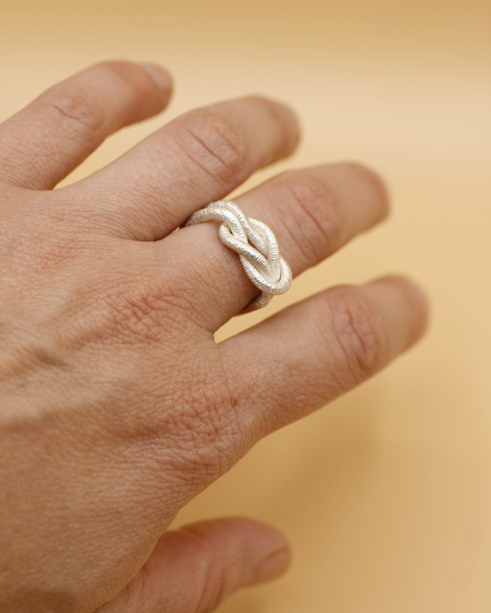 Ein Drei-Finger-Ring, der aussieht, wie ein dünnes Haargummi, das man über drei Finger spannt - hergestellt von Goldschmiedin Annie Sibert.