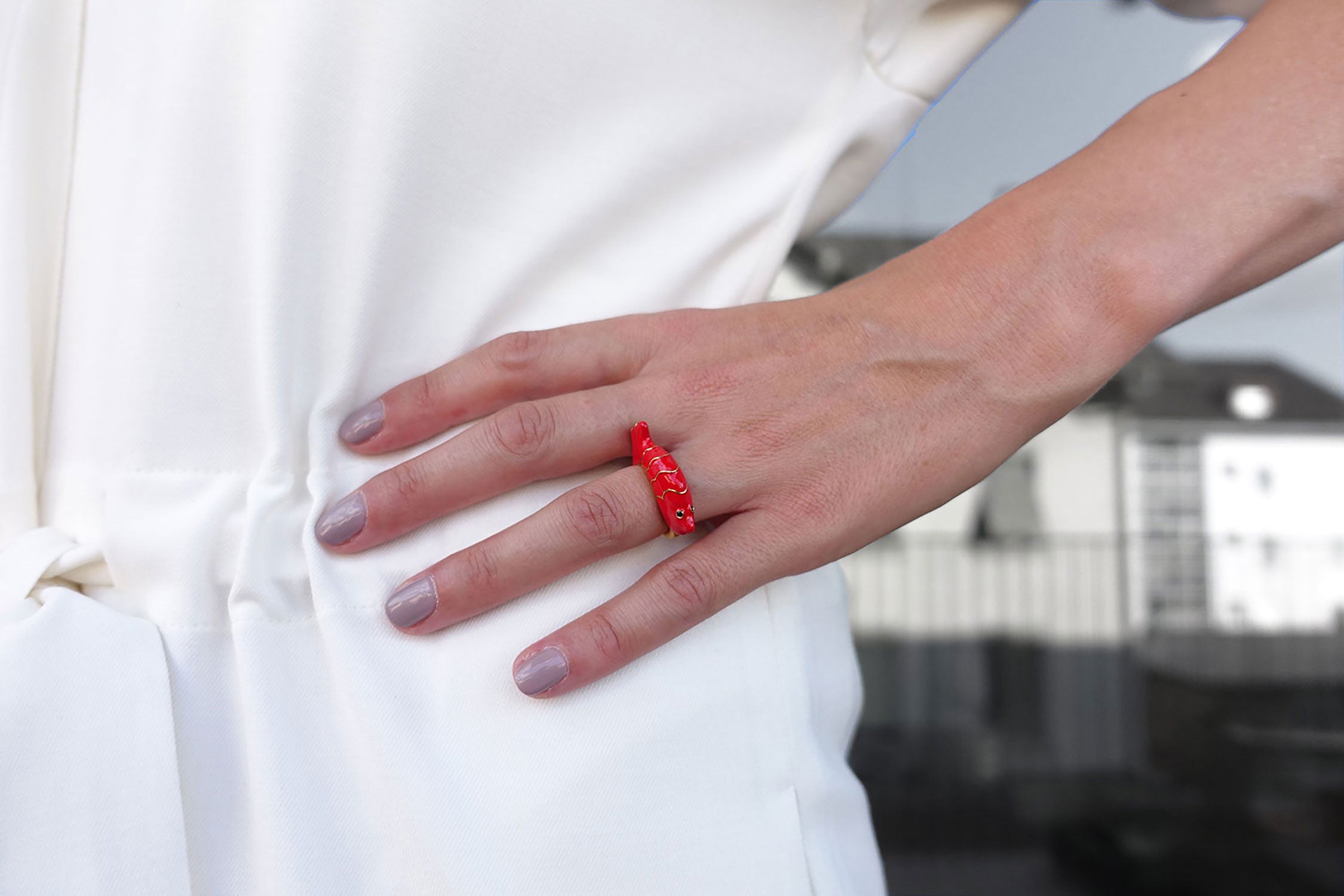 Eine Frau trägt einen Fingerring der italienischen Schmuckdesignerin Chiara Bello in Form eines roten Fischs mit goldenen Konturen und schwarzen Steinchen als Augen.
