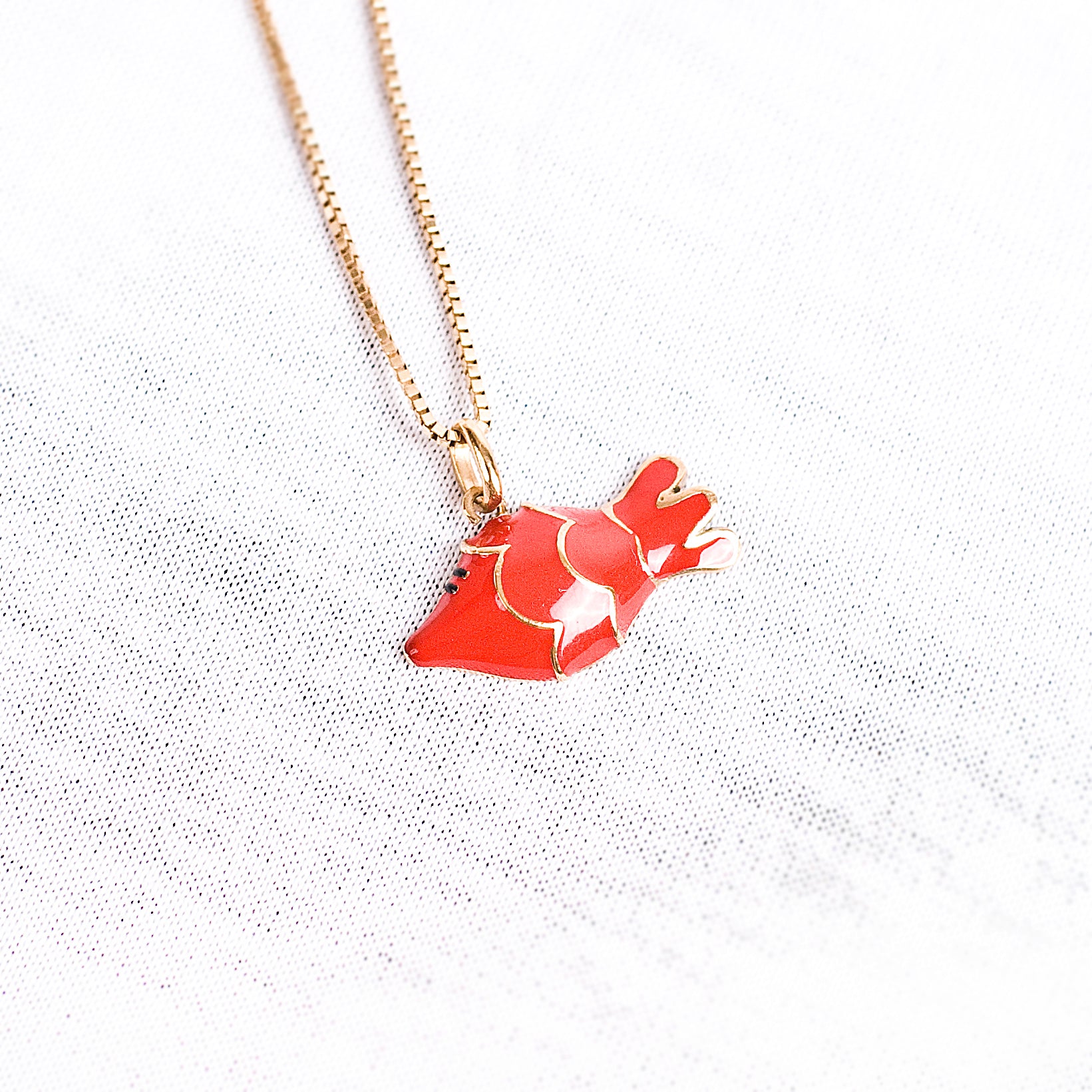 Eine schmale goldene Halskette mit einem Anhänger in Form einesrot-goldenen Fischs der italienischen Schmuckdesignerin Chiara Bello von chic pig.