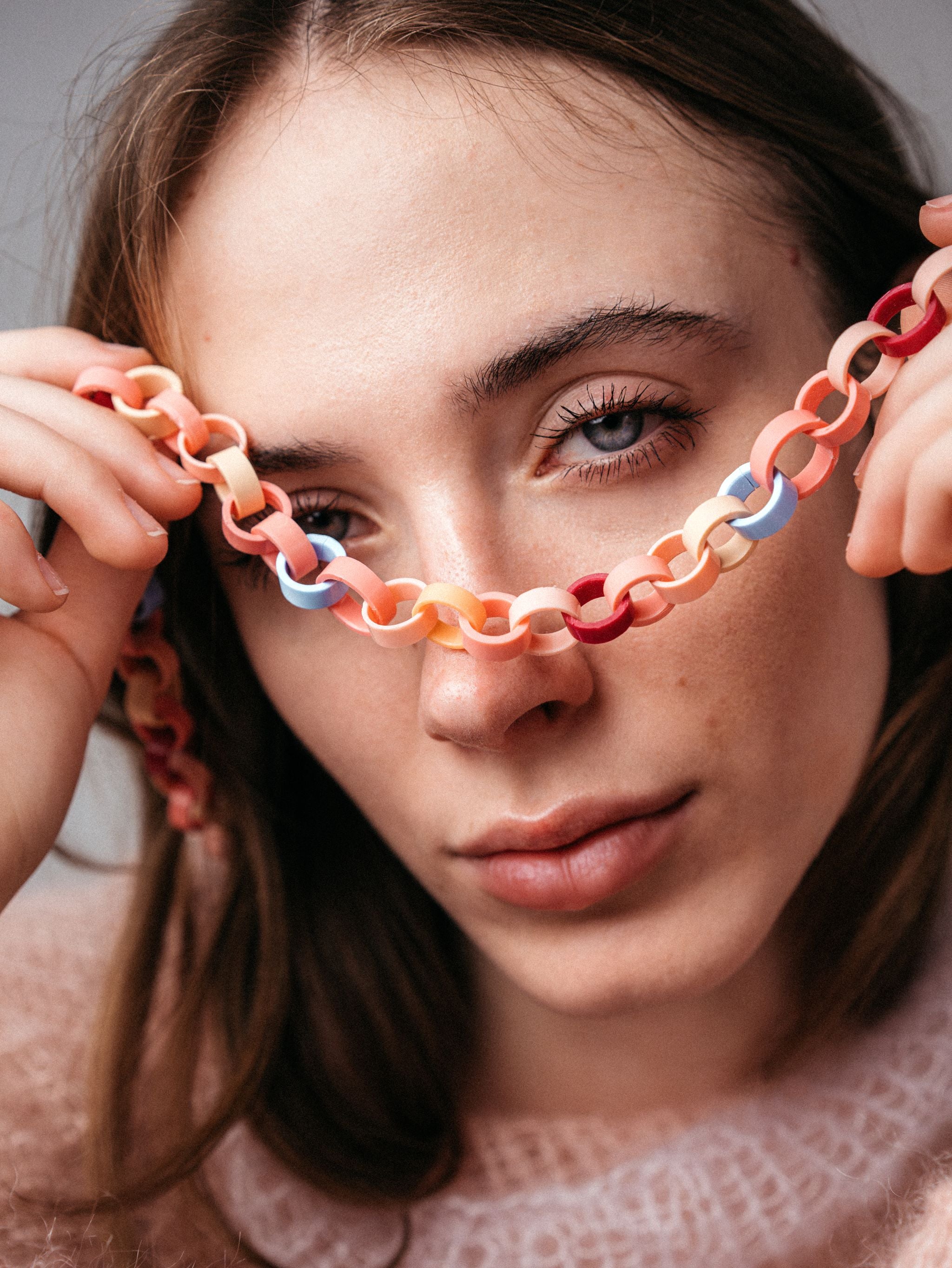 Ein Model trägt eine Gliederkette, deren Glieder in Rosa-, Rot, und Hellblautönen aus recyclten Hülsen von Filstiften bestehen.