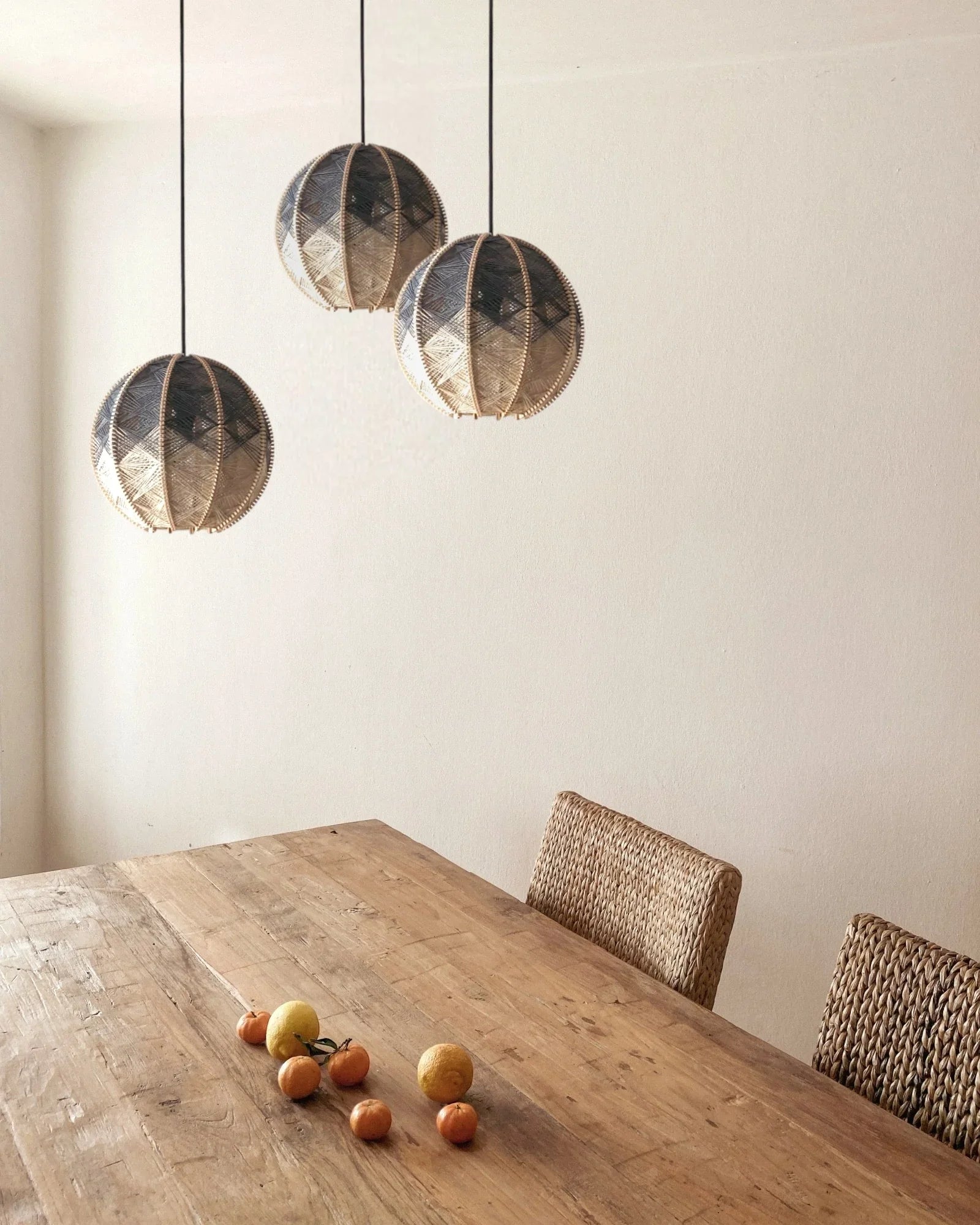 drei runde Hängeleuchten aus Birkenholz umwebt mit Leinengarn in Beige und Anthrazit hängen versetzt über einem Holztisch mit Zitrusfrüchten