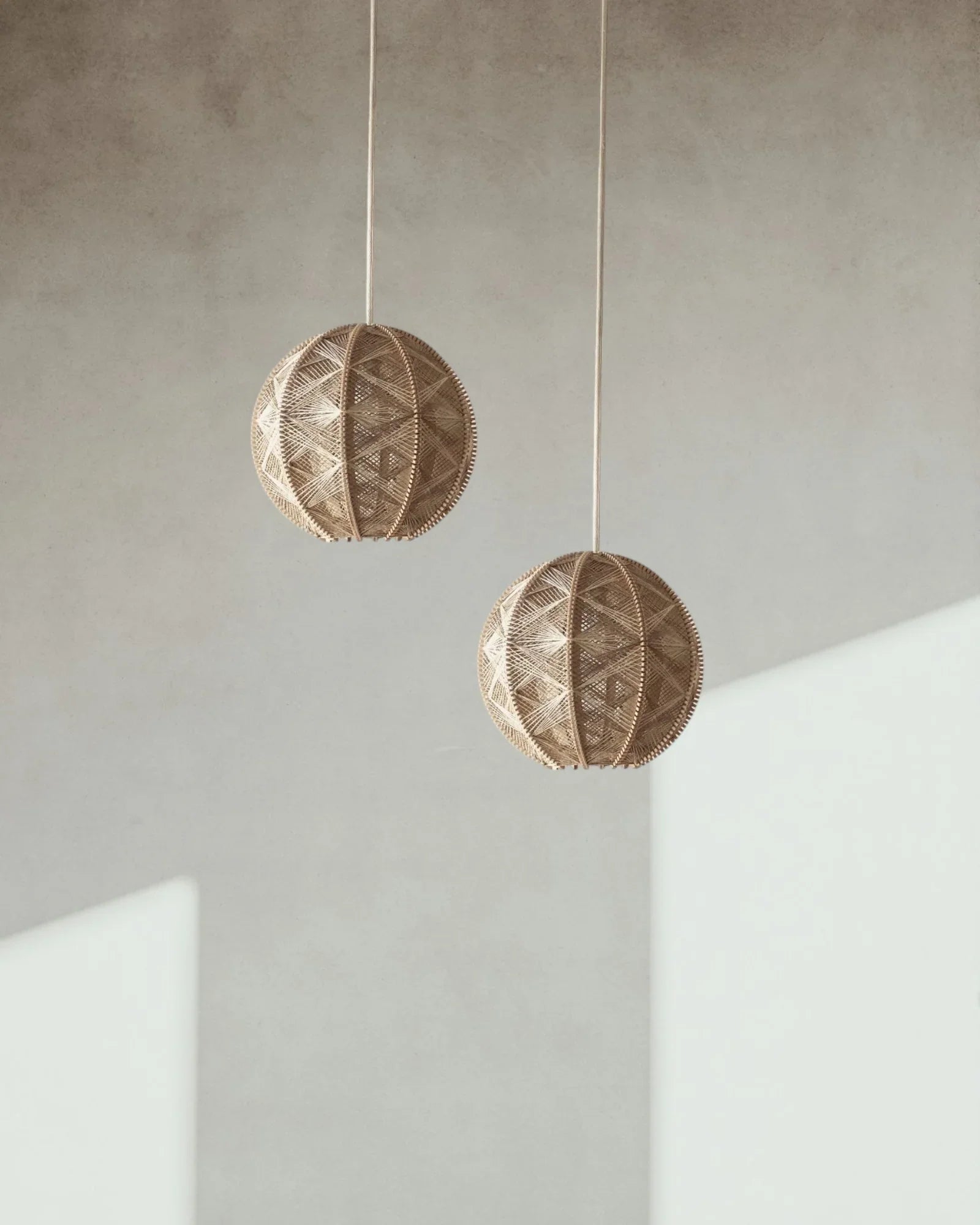 zwei runde Hängeleuchten aus Birkenholz umwebt mit beigem Leinengarn hängen versetzt vor einer Wand
