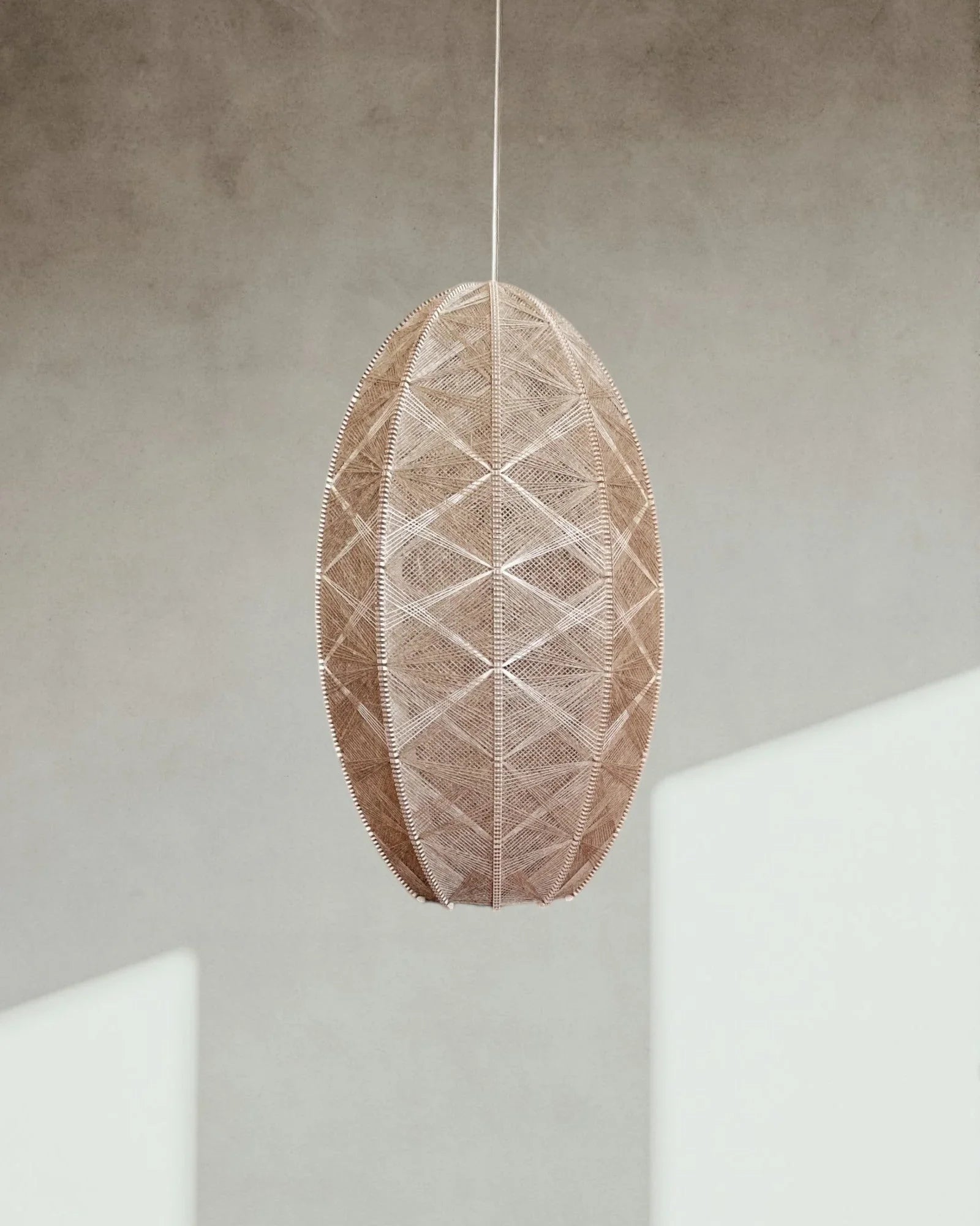 eine zylindrische Hängelampe aus Birkenholz und Leinengarn hängt vor einer Wand mit Schatten