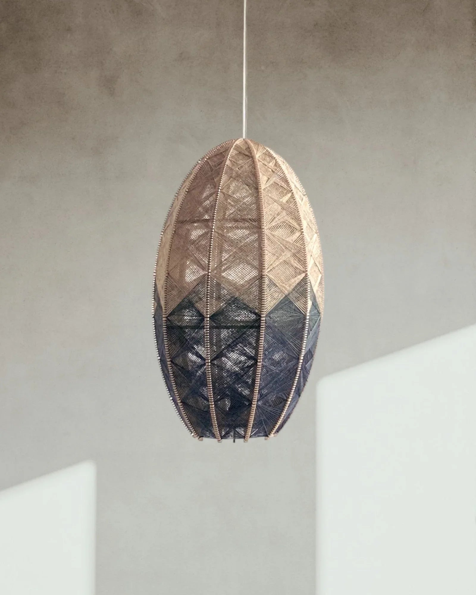 eine zylindrische Hängelampe aus Birkenholz und Leinengarn hängt vor einer Wand mit Schatten