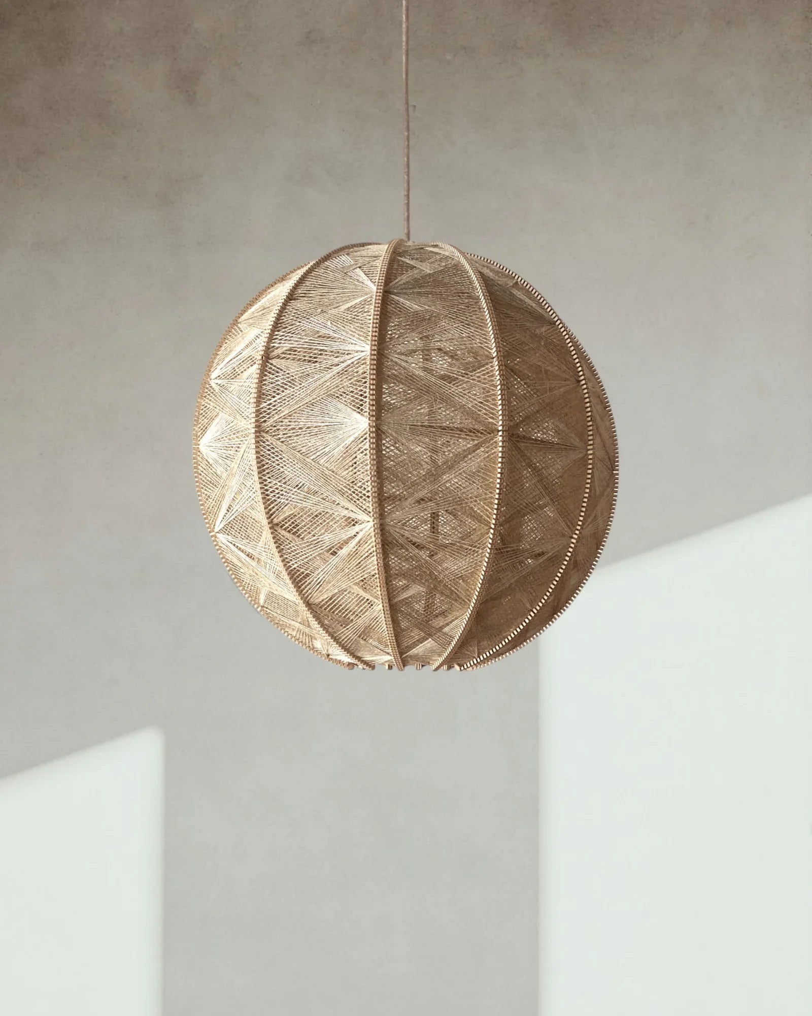 eine runde Hängeleuchte aus Birkenholz umwebt mit Leinengarn in Beige hängt vor einer Wand