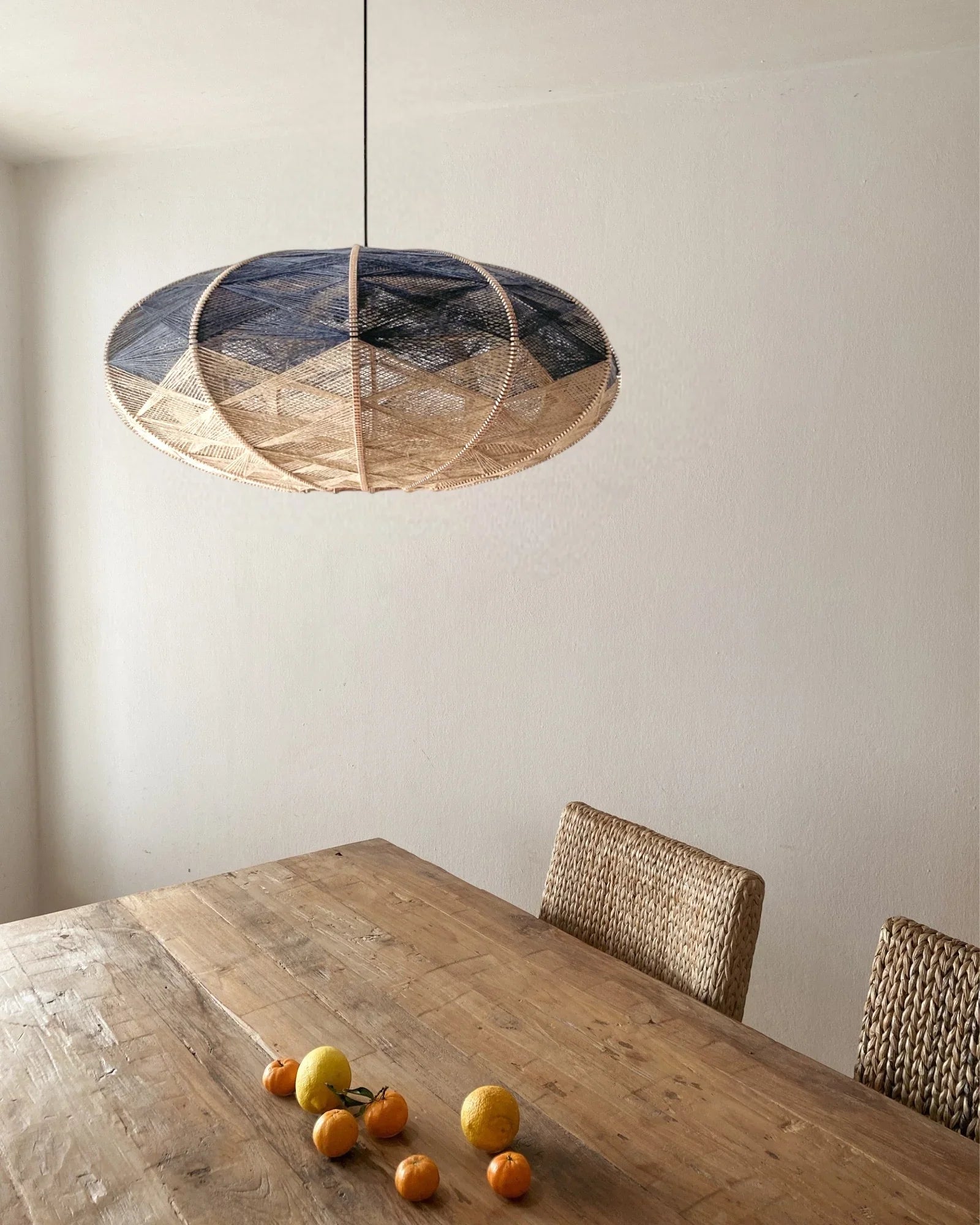 eine elliptische Hängeleuchte aus Birkenholz umwebt mit Leinengarn in Beige und Anthrazit hängt über einem Esstisch mit Zitrusfrüchten