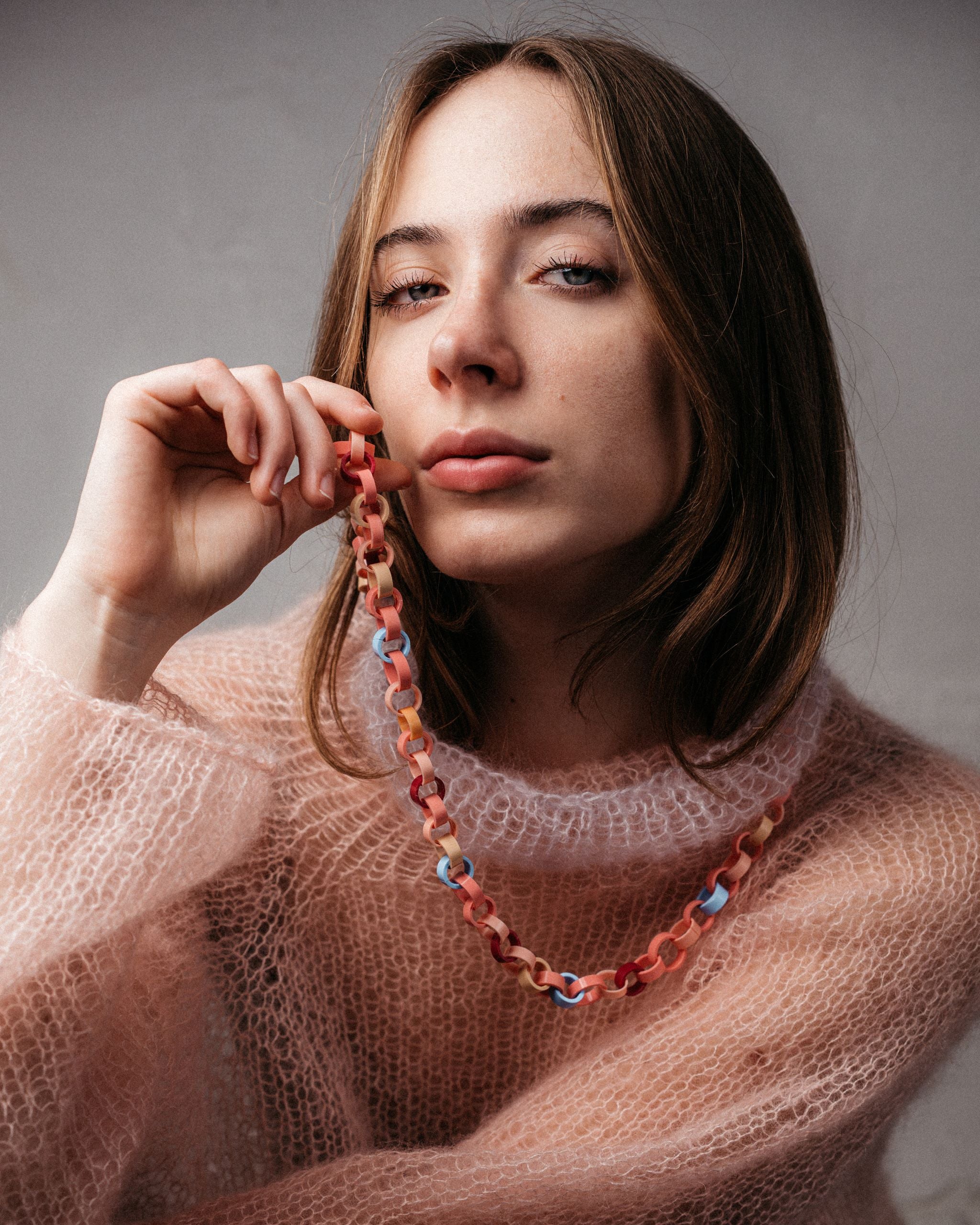 Ein Model trägt eine Gliederkette, deren Glieder in Rosa-, Rot, und Hellblautönen aus recyclten Hülsen von Filstiften bestehen.