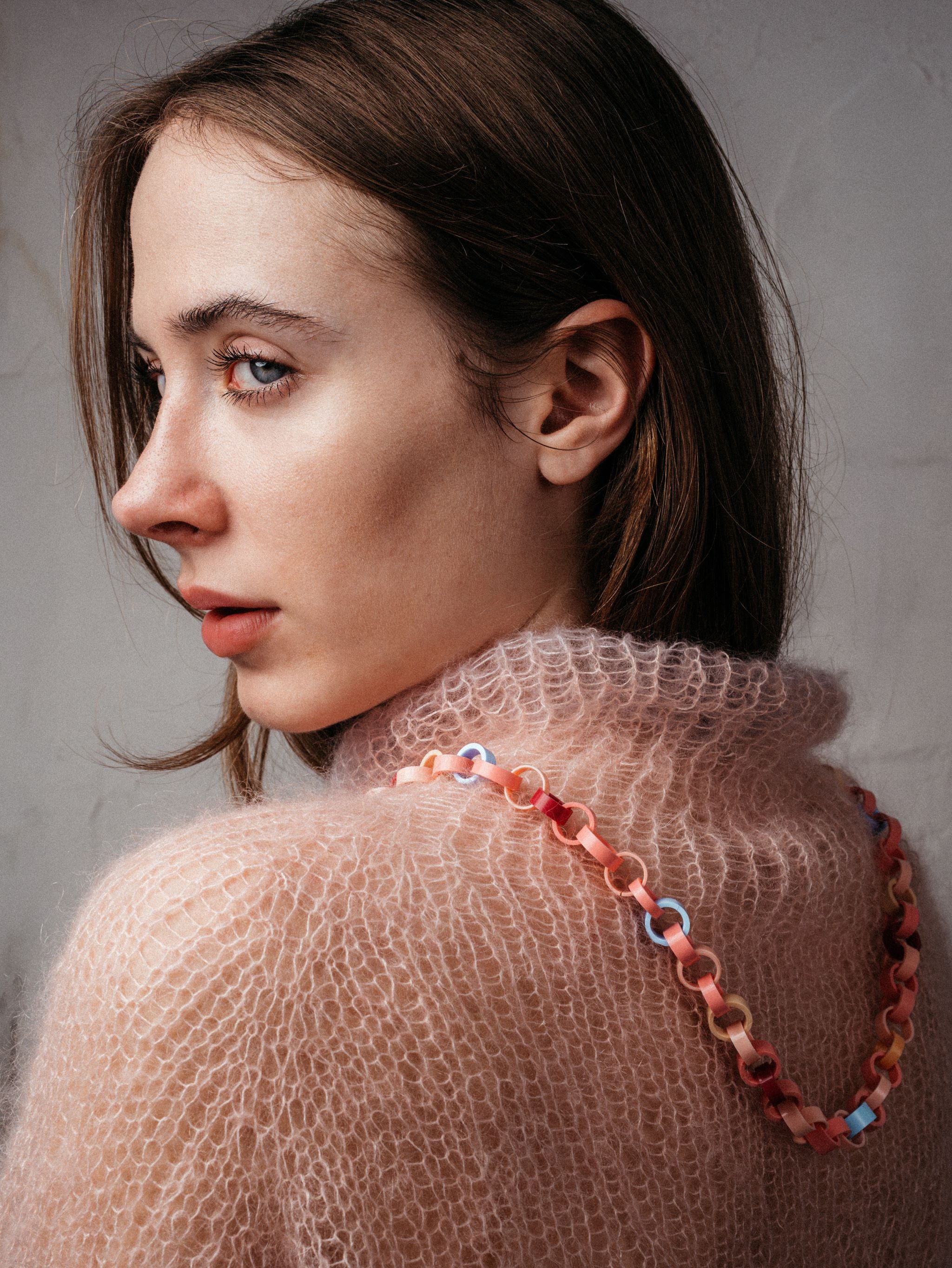 Ein Model trägt eine Gliederkette, deren Glieder in Rosa-, Rot, und Hellblautönen aus recyclten Hülsen von Filstiften bestehen.