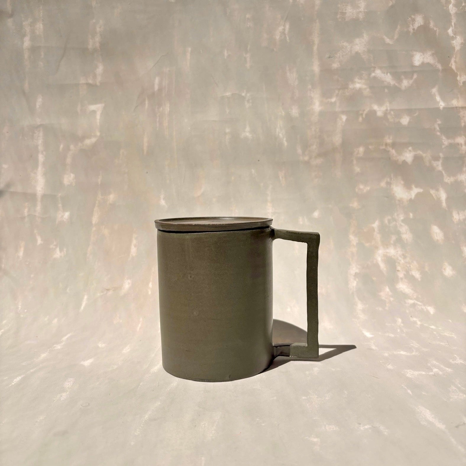 Eine Kermiktasse mit rechteckigem Henkel und Deckel, der zugleich Untersetzer ist, hergestellt von der genueser Künstlerin Martina Geroni.