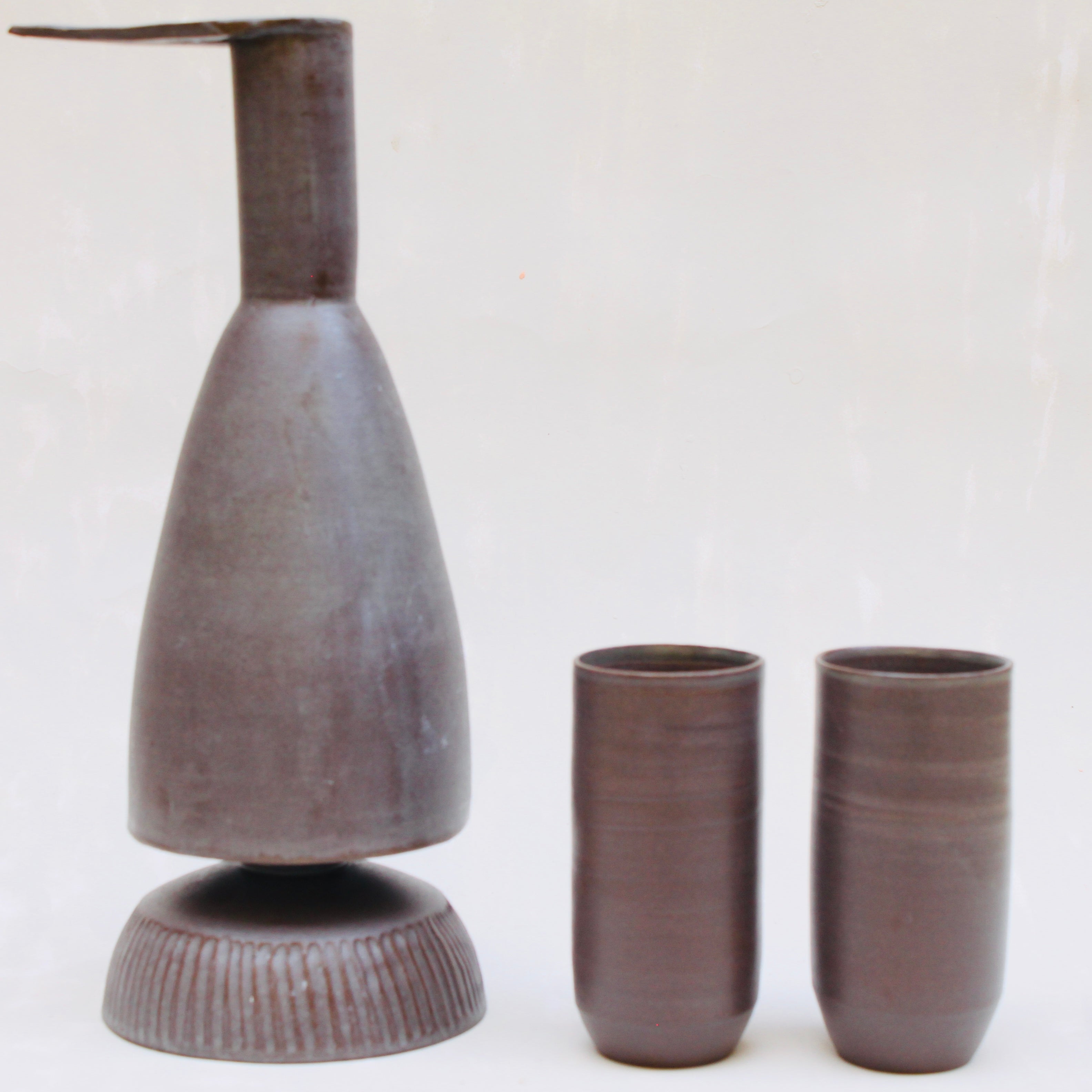 Eine Keramikkaraffe in Form eines stilisierten Reihers, mit einem abnehmbaren Schälchen als Fuss und zwei schlanken Bechern im Set.