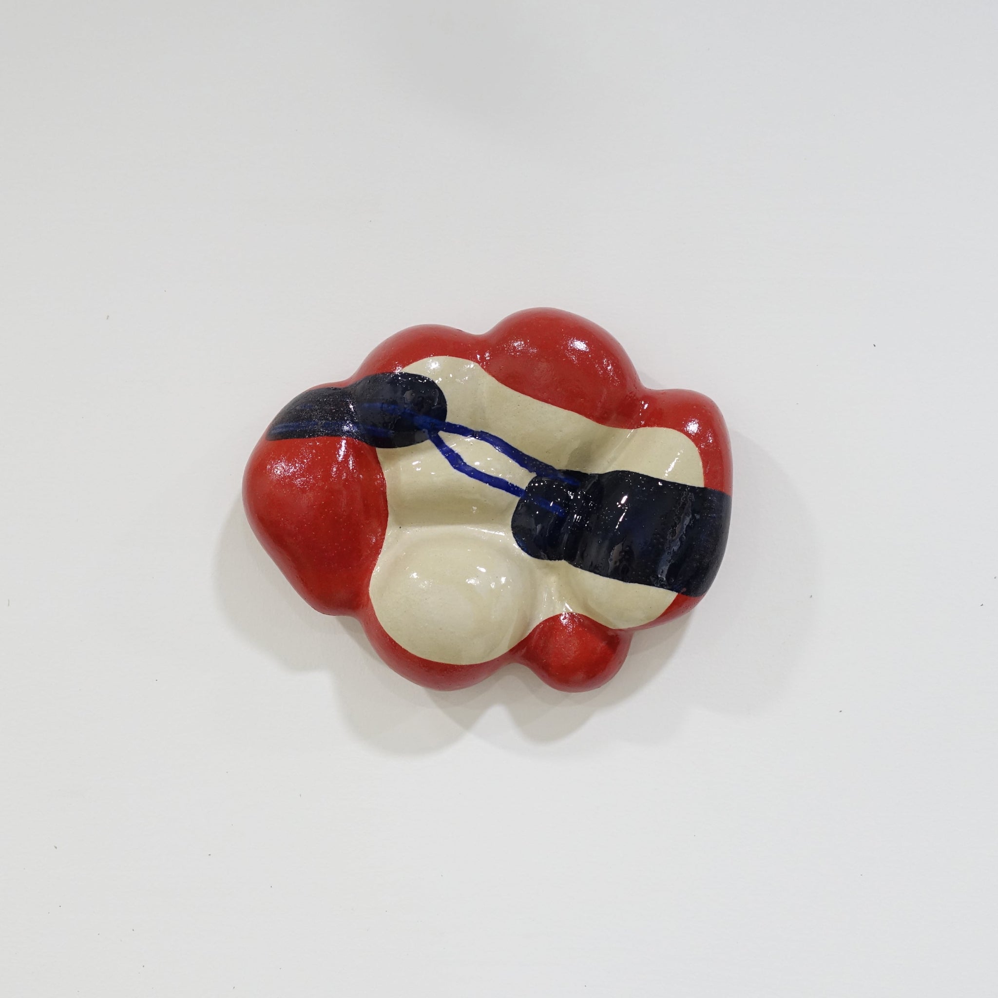 Keramische Wandskulptur mit organisch gewölbter Form; cremefarbener Grundton mit leuchtend roten Flächen sowie dunkelblauen, gestischen Linien- und Flächenakzenten auf der Oberfläche.