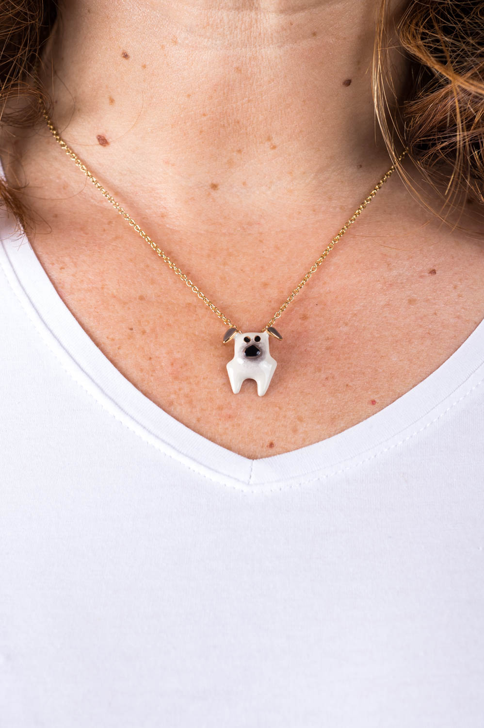 Eine Frau trägt eine schmale goldene Halskette mit einem Anhänger in Form eines weissen Mops mit grauen Ohren und schwarzer Schnauze der italienischen Schmuckdesignerin Chiara Bello von chic pig.