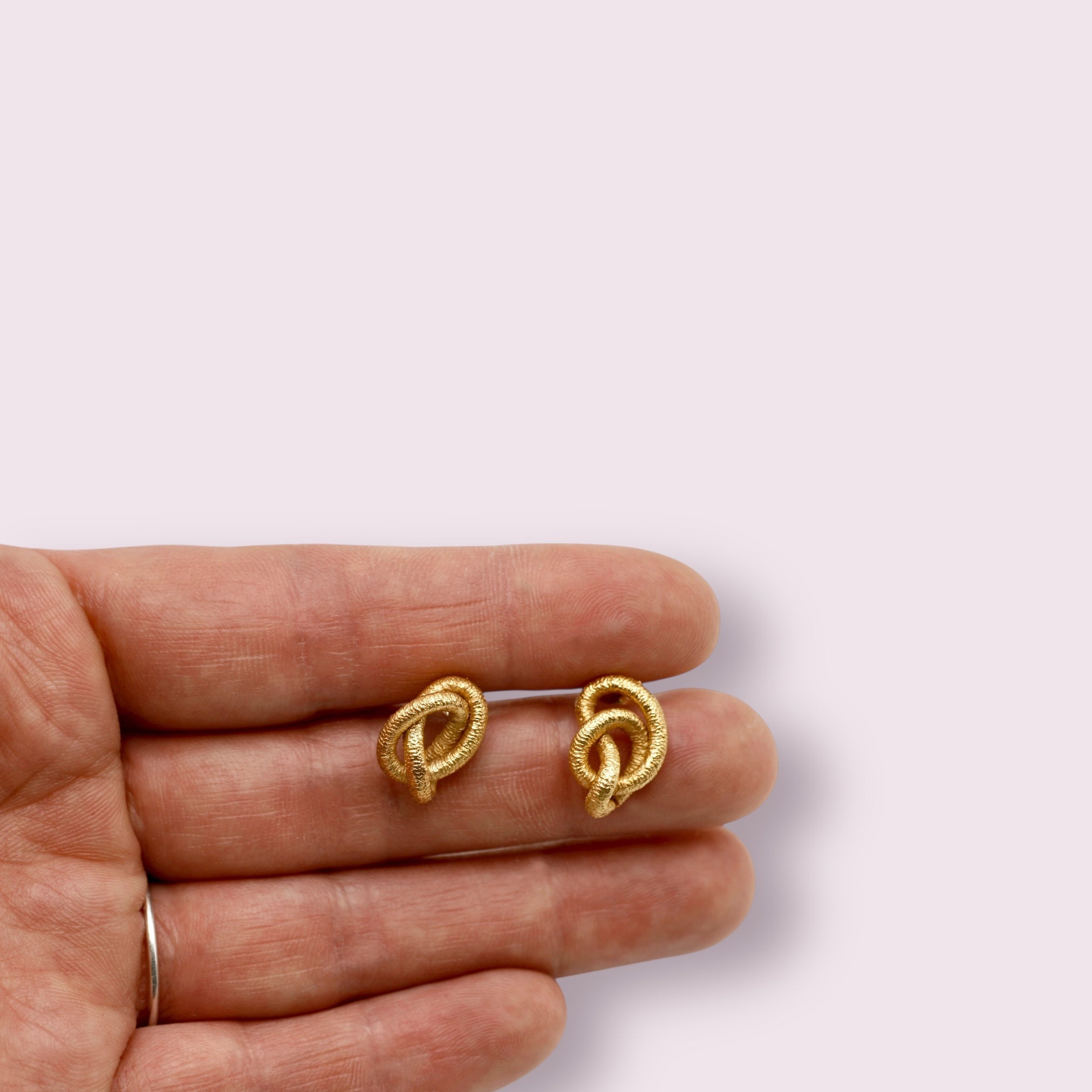 Eine Hand hält zwei goldene Ohrstecker in Knotenform.
