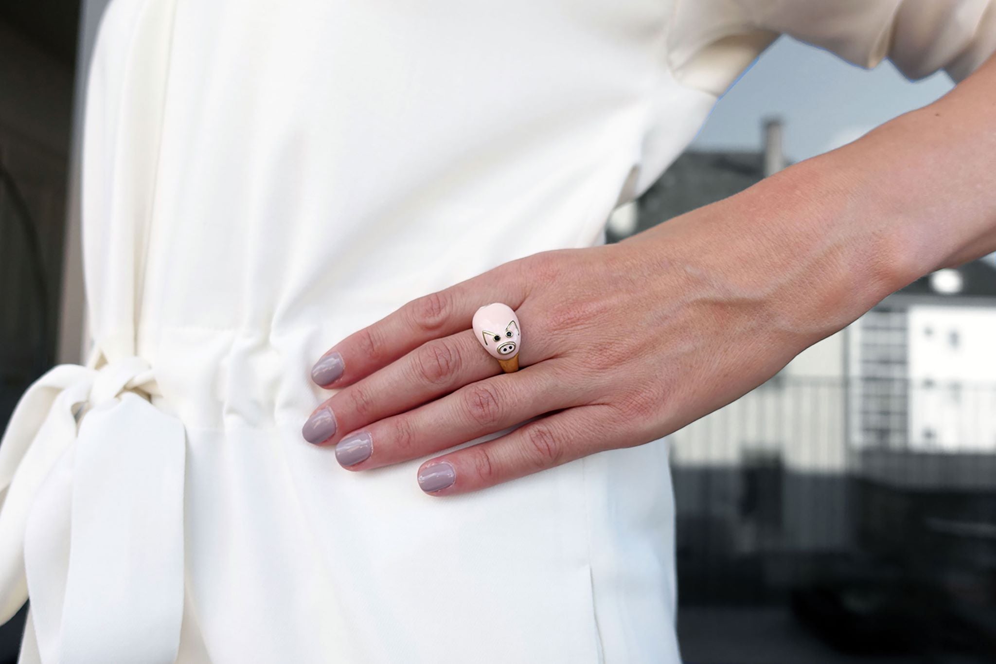 Eine Frau trägt einen Fingerring der italienischen Schmuckdesignerin Chiara Bello in Form eines rosa Schweinchens mit goldenen Ohren und schwarzen Steinchen als Augen.
