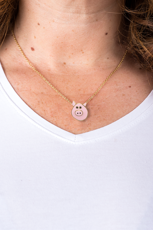 Eine Frau trägt eine schmale goldene Halskette mit einem Anhänger in Form eines kleinen cshweinekopfs mit schwarzen Augen und goldenen Konturen der italienischen Schmuckdesignerin Chiara Bello von chic pig.
