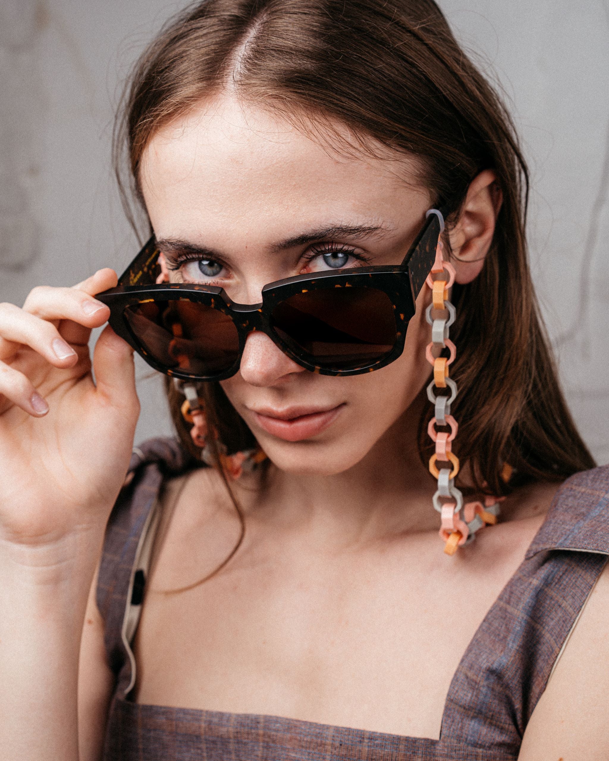 Ein Model trägt an einer großen Sonnenbrille eine Gliederkette mit achteckigen Gliedern in pastelligen Tönen, die aus den Hülsen alter Filzstifte bestehen.