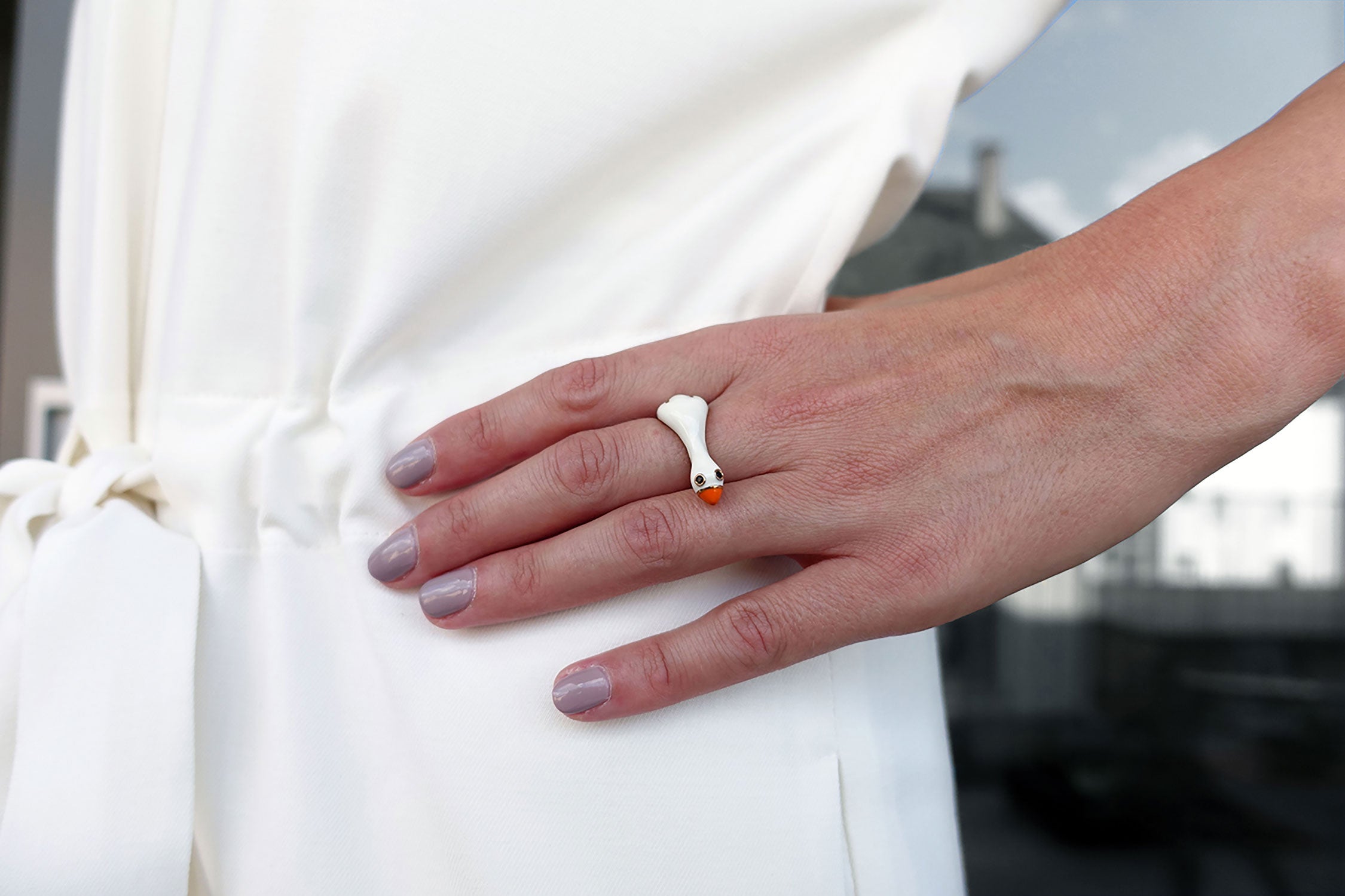 Eine Frau trägt einen Fingerring der italienischen Schmuckdesignerin Chiara Bello in Form einer weissen Gans mit orangem Schnabel und goldenen Konturen.