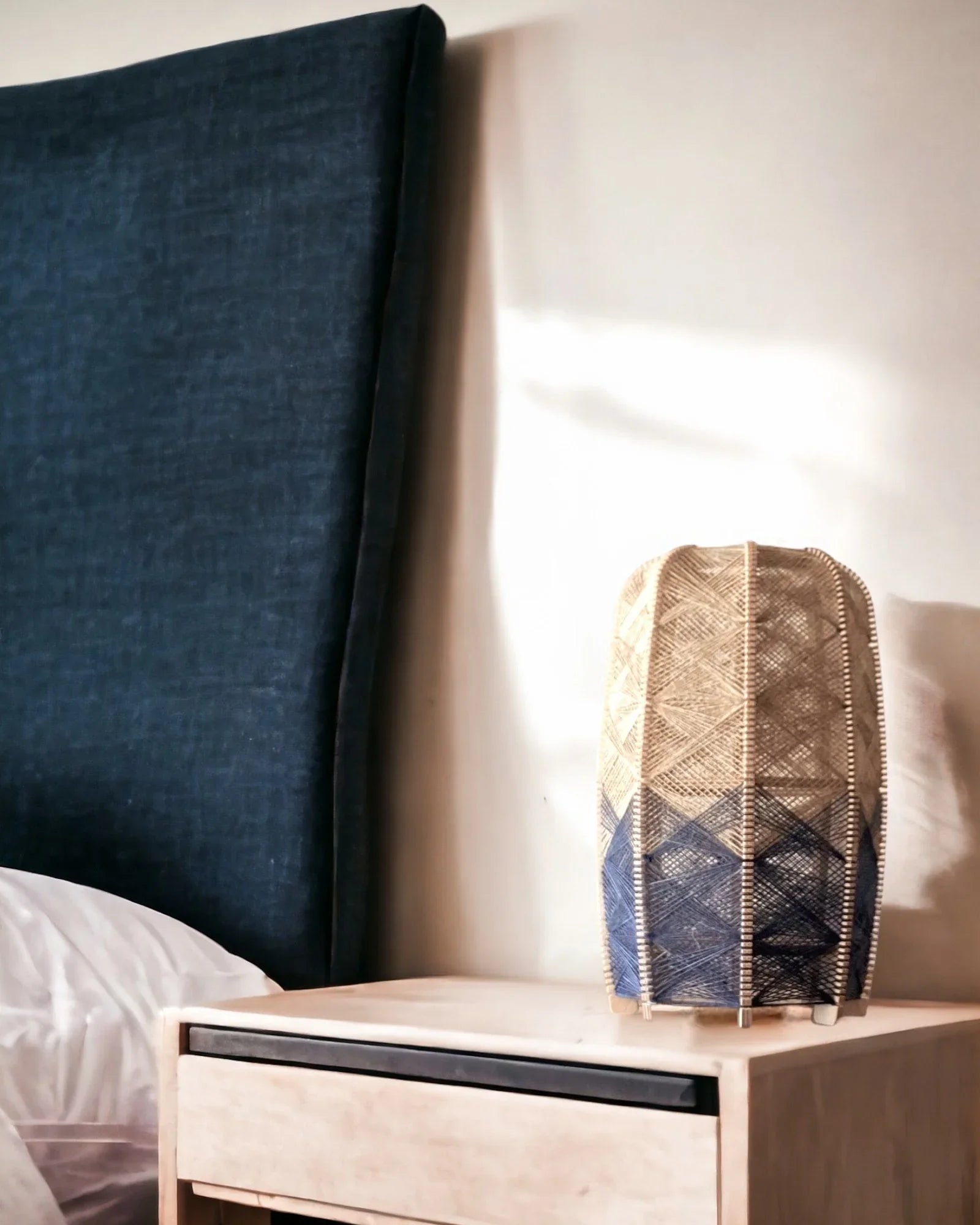 ein gewebter Lampenschirm aus Birkenholz und Leinengarn in Beige und Anthrazit steht auf einem Nachtisch neben einem Bett