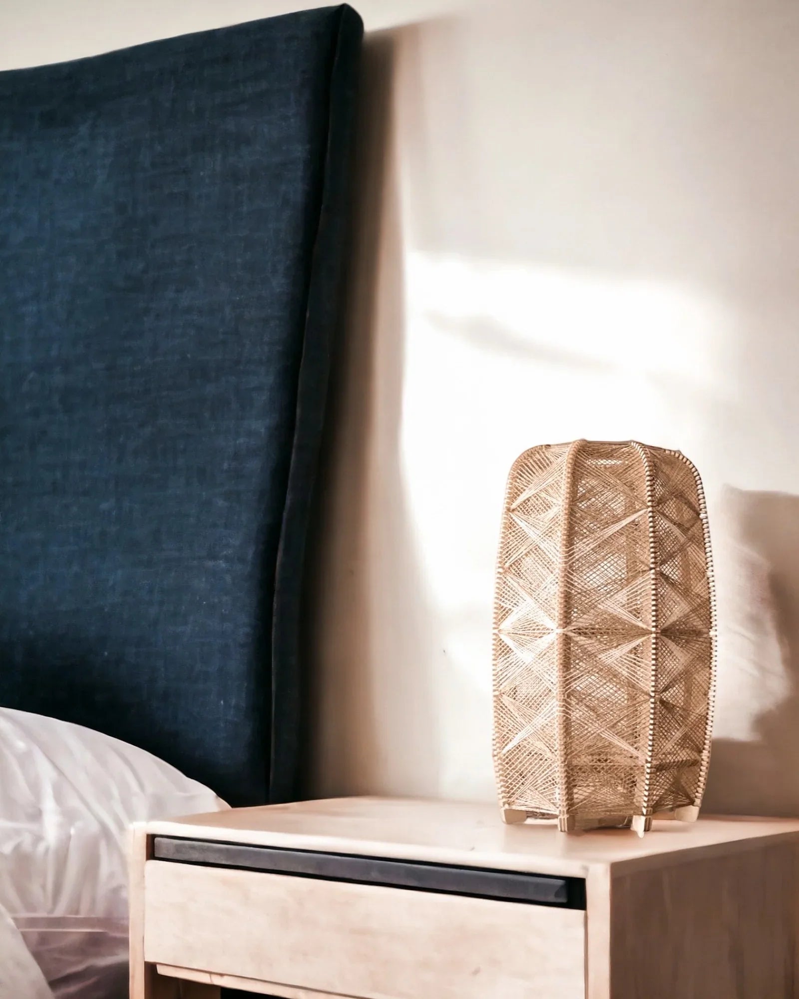 eine zylindrisch Tischleuchte aus Birkenholz und gewebtem Leinengarn in Beige steht auf einem Nachtisch neben einem Bett