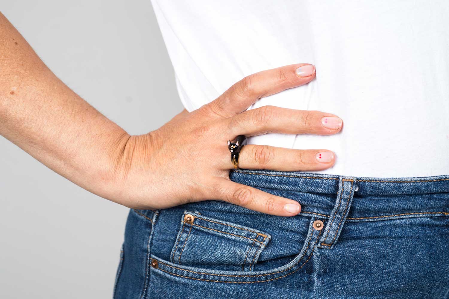 Eine Frau trägt einen Fingerring der italienischen Schmuckdesignerin Chiara Bello in Form einer schwarzen Katze mit rose Ohren und Schnauze, goldenen Konturen und schwarzen Steinchen als Augen.