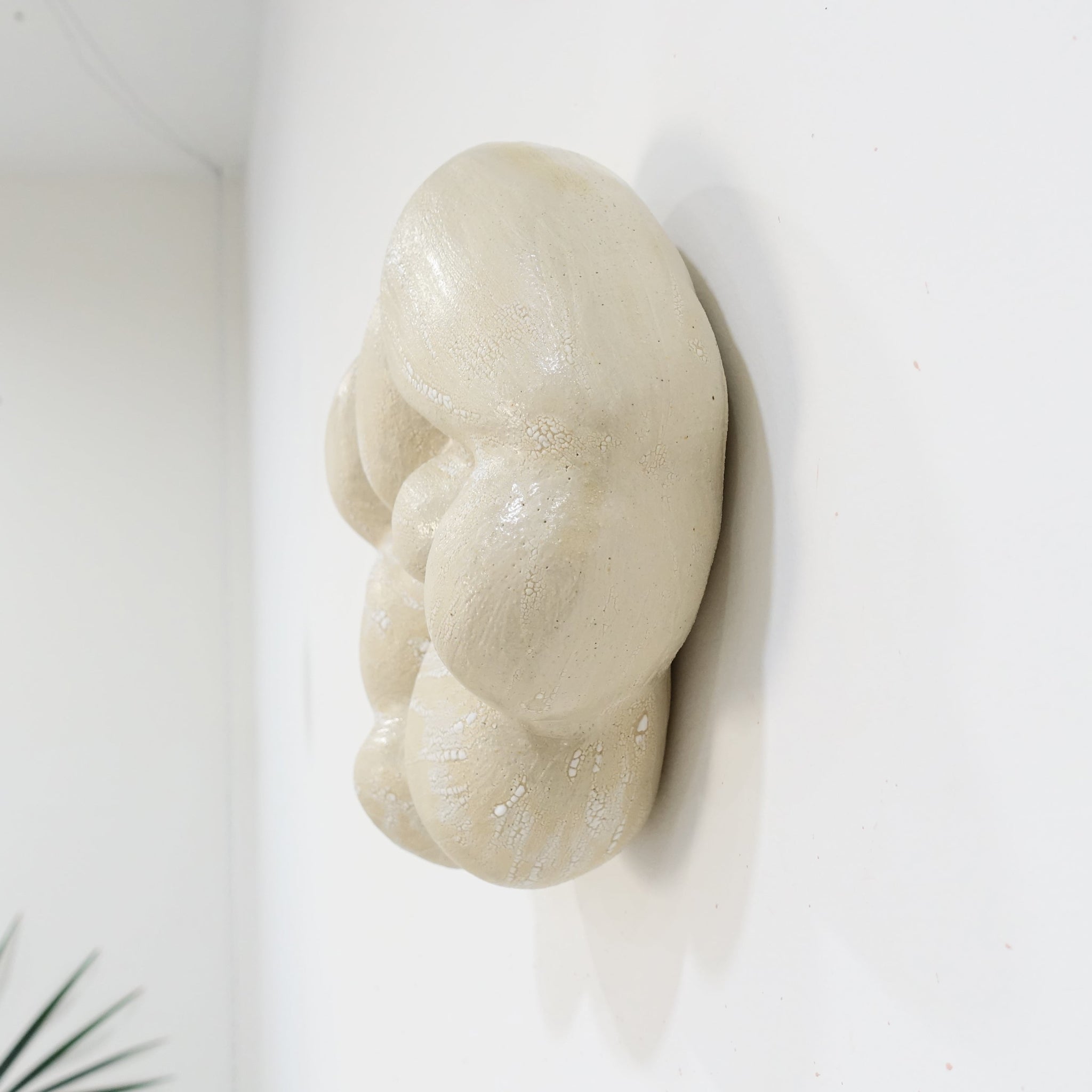 Seitenansicht einer Wandskulptur aus Keramik in organischer, wolkenartiger Form; helle, leicht cremeweiße Oberfläche mit feinen Rissstrukturen und weicher, gewölbter Modellierung.