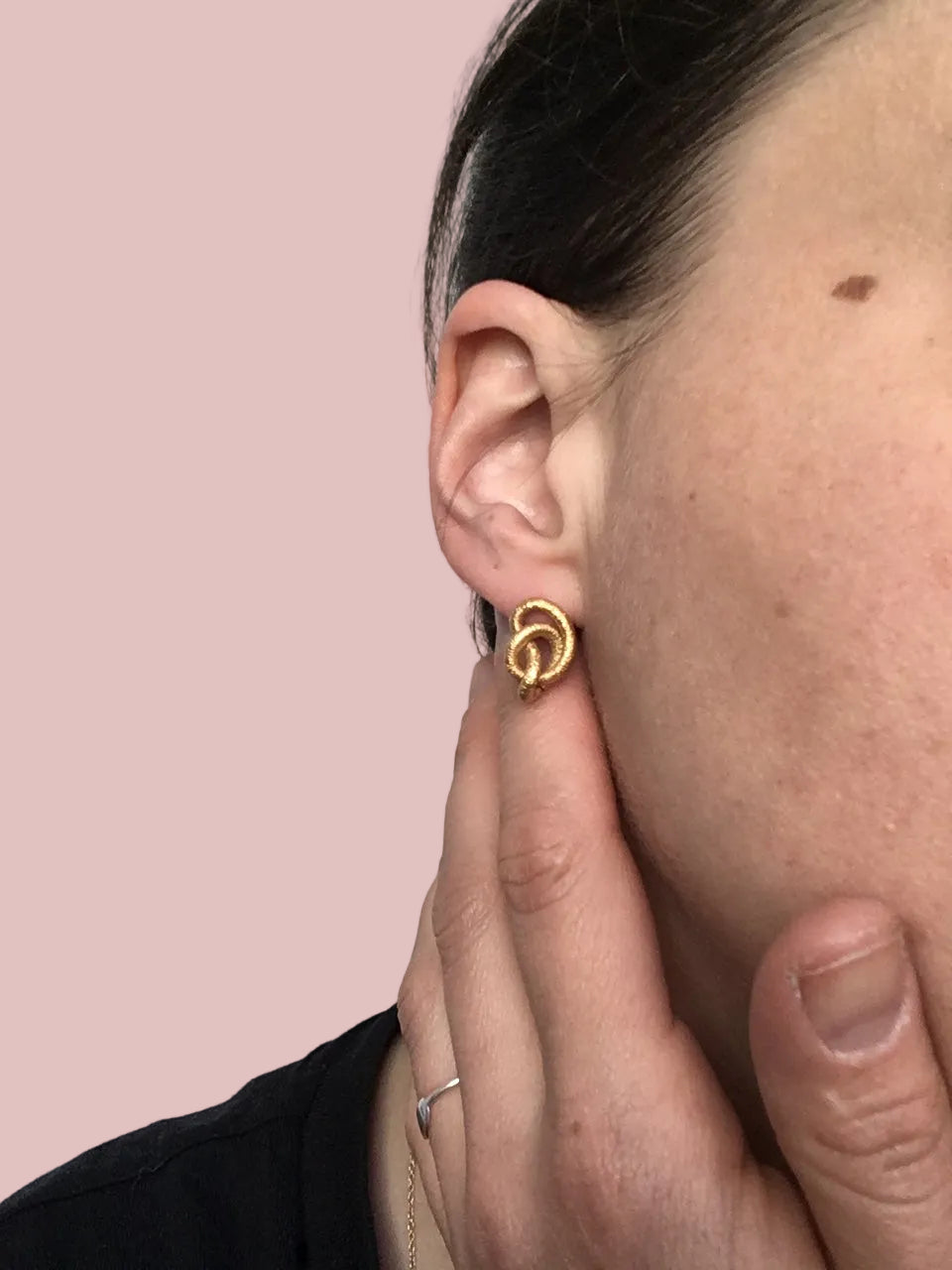 Ein goldener Ohrring in Knotenform am Seitenprofil einer Person mit dunklen Haaren.