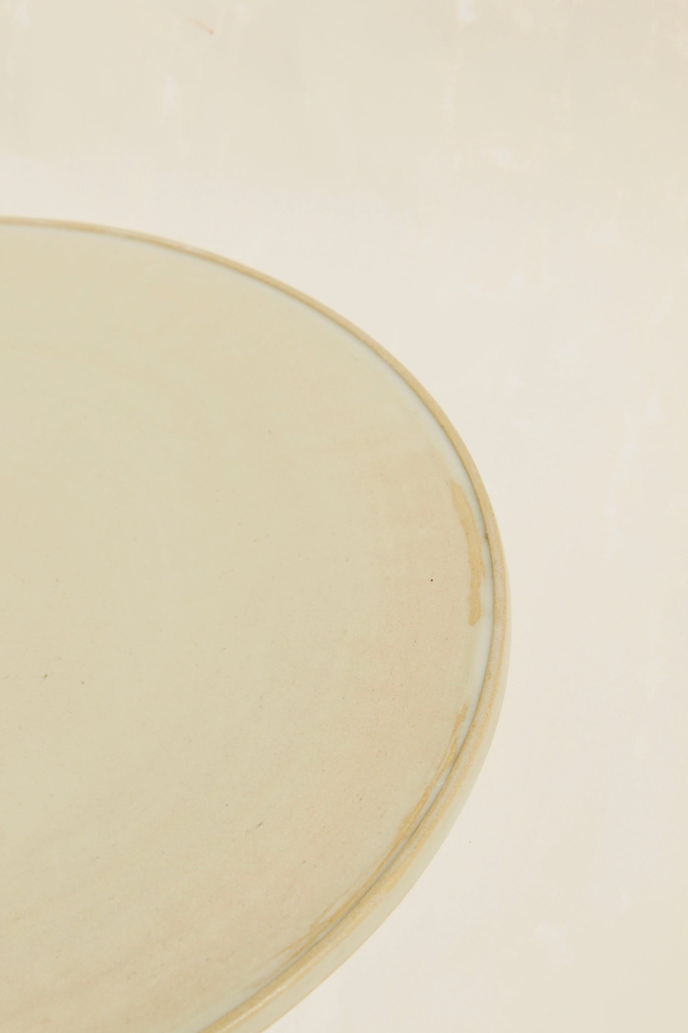 Detailansicht des modularen Pizzatellers aus der Kollektion ROSA MORADA von Martina Geroni in der Tonfarbe Fiore di Cotone, gefertigt aus Steingut, mit minimal erhöhtem Rand auf hellem Hintergrund.