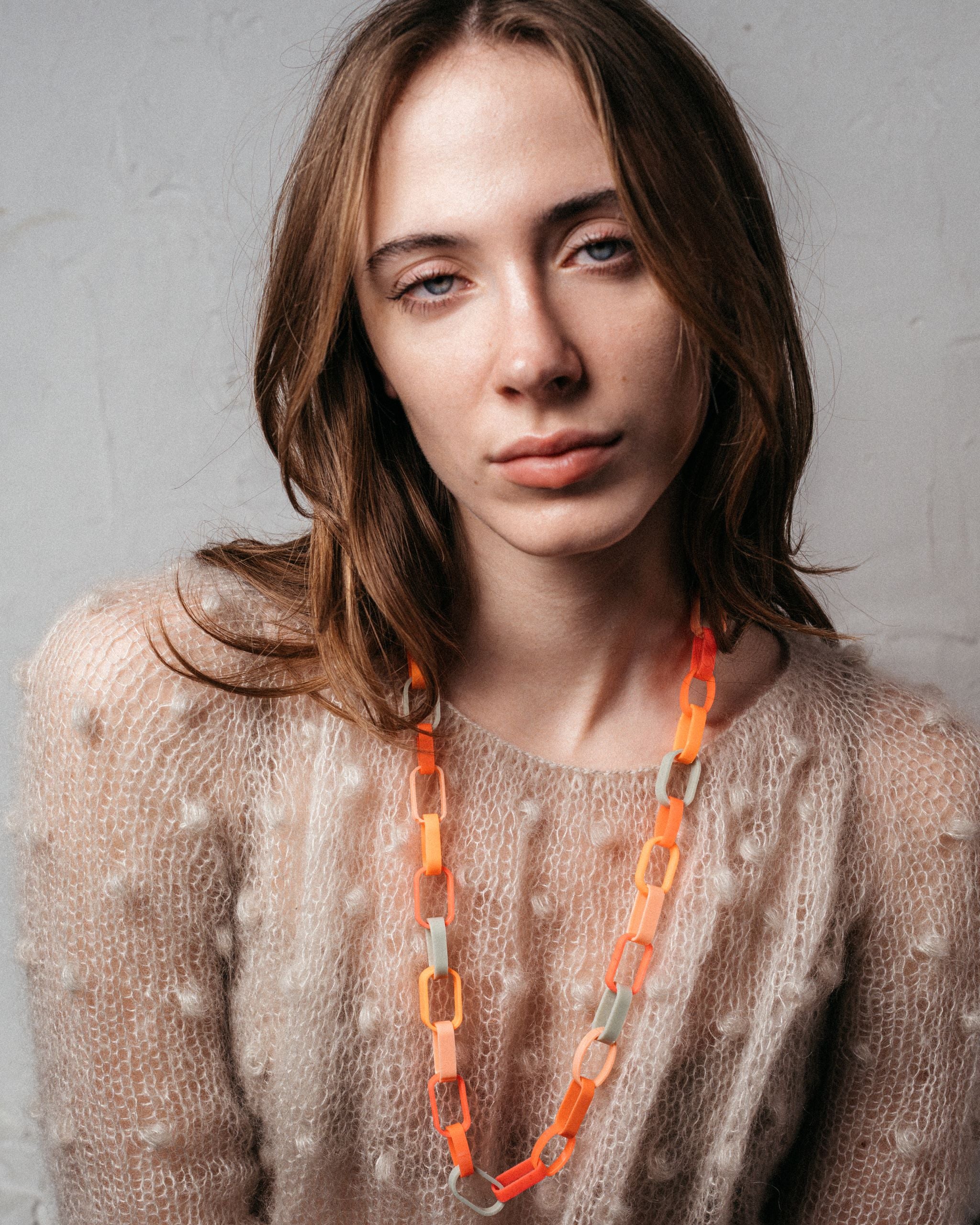 Ein Model trägt eine Gliederkette der Schmuckdesignerin Carla Movia, deren große Glieder in herbstlich leuchtenden Farben aus recyclten Hülsen von Textmarkern bestehen.