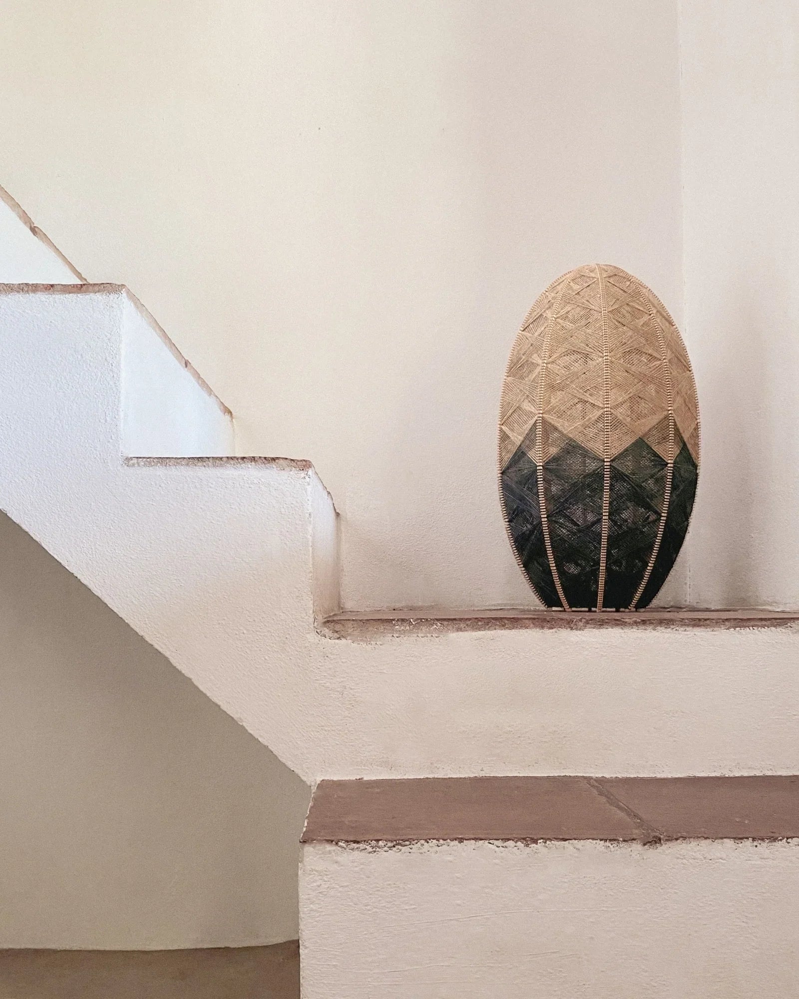 eine handgewebte Lampe aus Birkenholz und Leinengarn in Beige und Anthrazit auf einer mediterranen Treppe