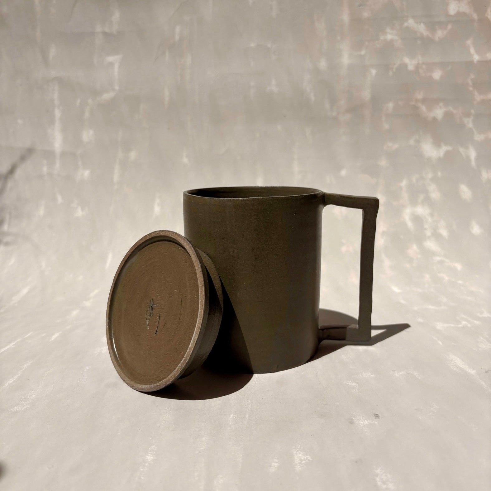 Eine Kermiktasse mit rechteckigem Henkel und Deckel, der zugleich Untersetzer ist, hergestellt von der genueser Künstlerin Martina Geroni.