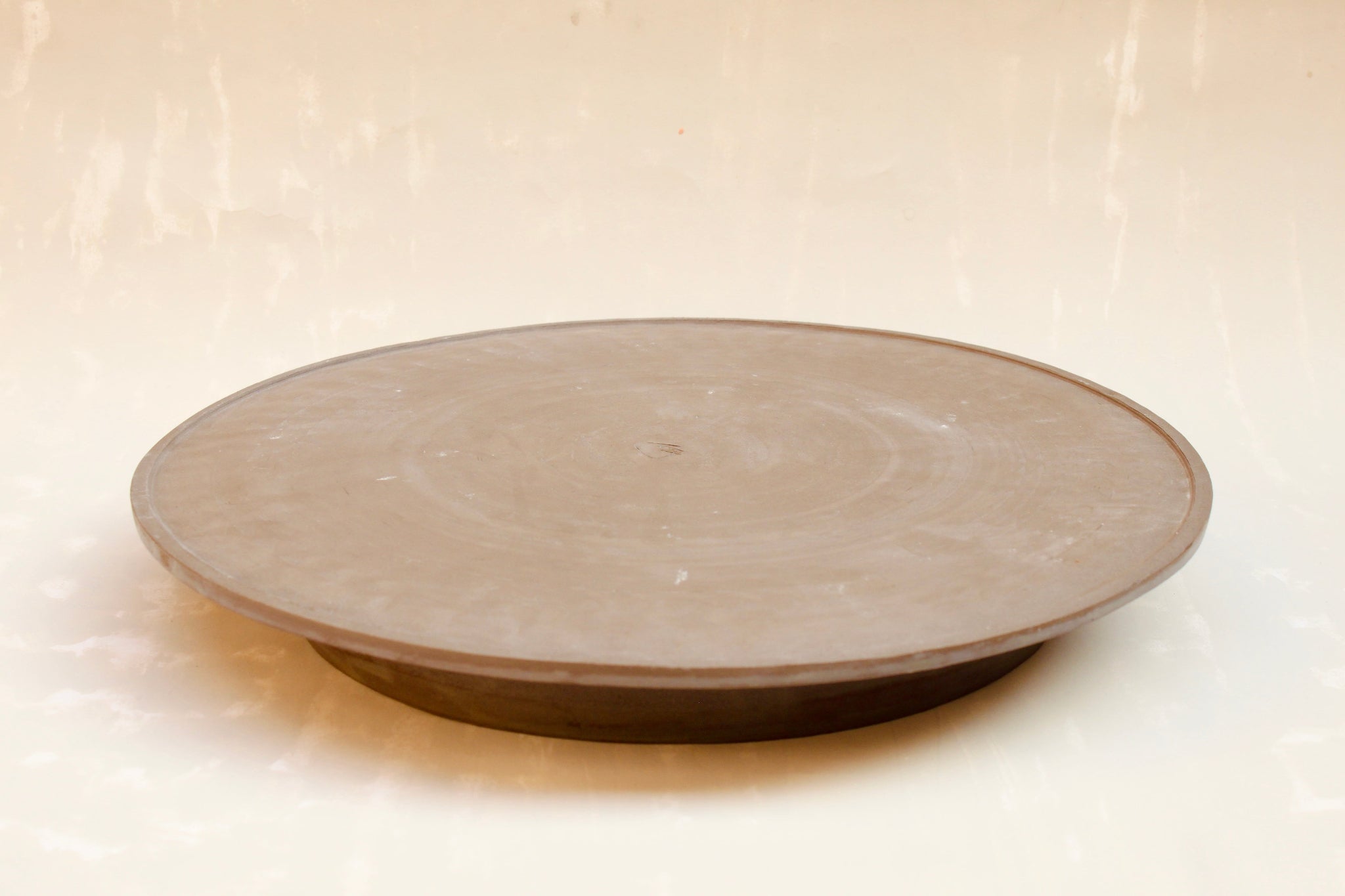 Großer flacher Teller aus der Kollektion ROSA MORADA von Martina Geroni in der Tonfarbe Buccia di Zenzero, handgefertigt aus Steingut, mit leicht erhöhtem Rand und sichtbaren Drehscheibenspuren.