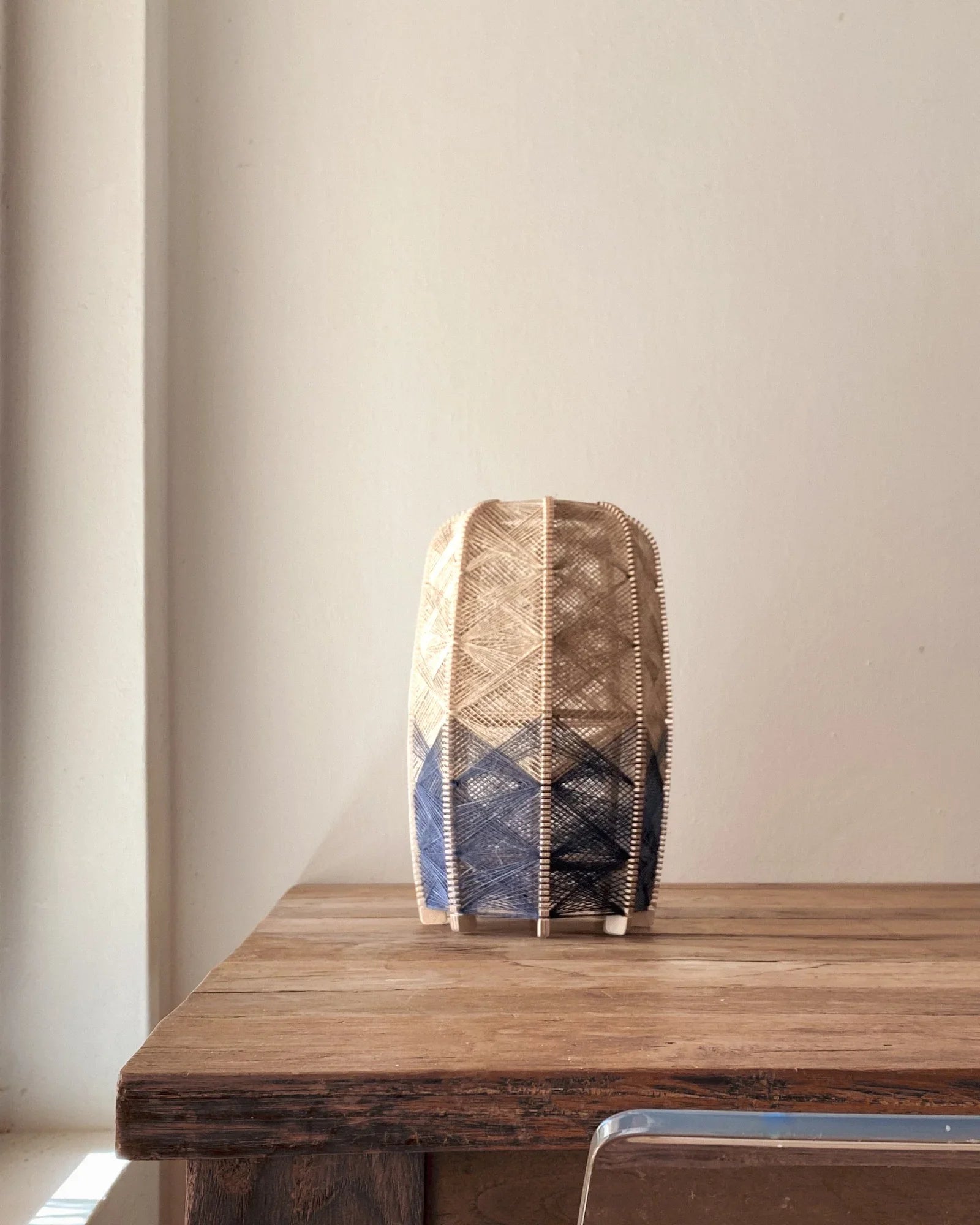 eine zylindrisch Tischleuchte aus Birkenholz und gewebtem Leinengarn in Beige und Anthrazit steht auf einem Holztisch
