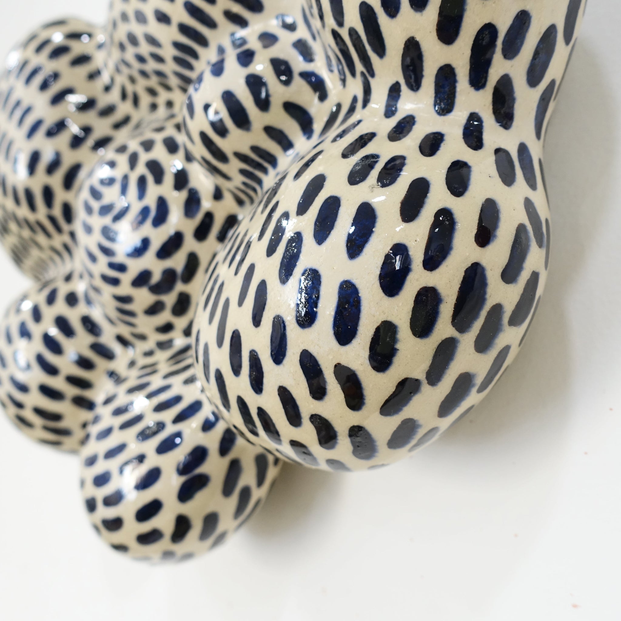 Detailansicht einer Wandskulptur mit organisch gewölbter, wolkenähnlicher Form; helles Grundmaterial, dicht überzogen mit gleichmäßig verteilten dunkelblauen Pinselstrichen.