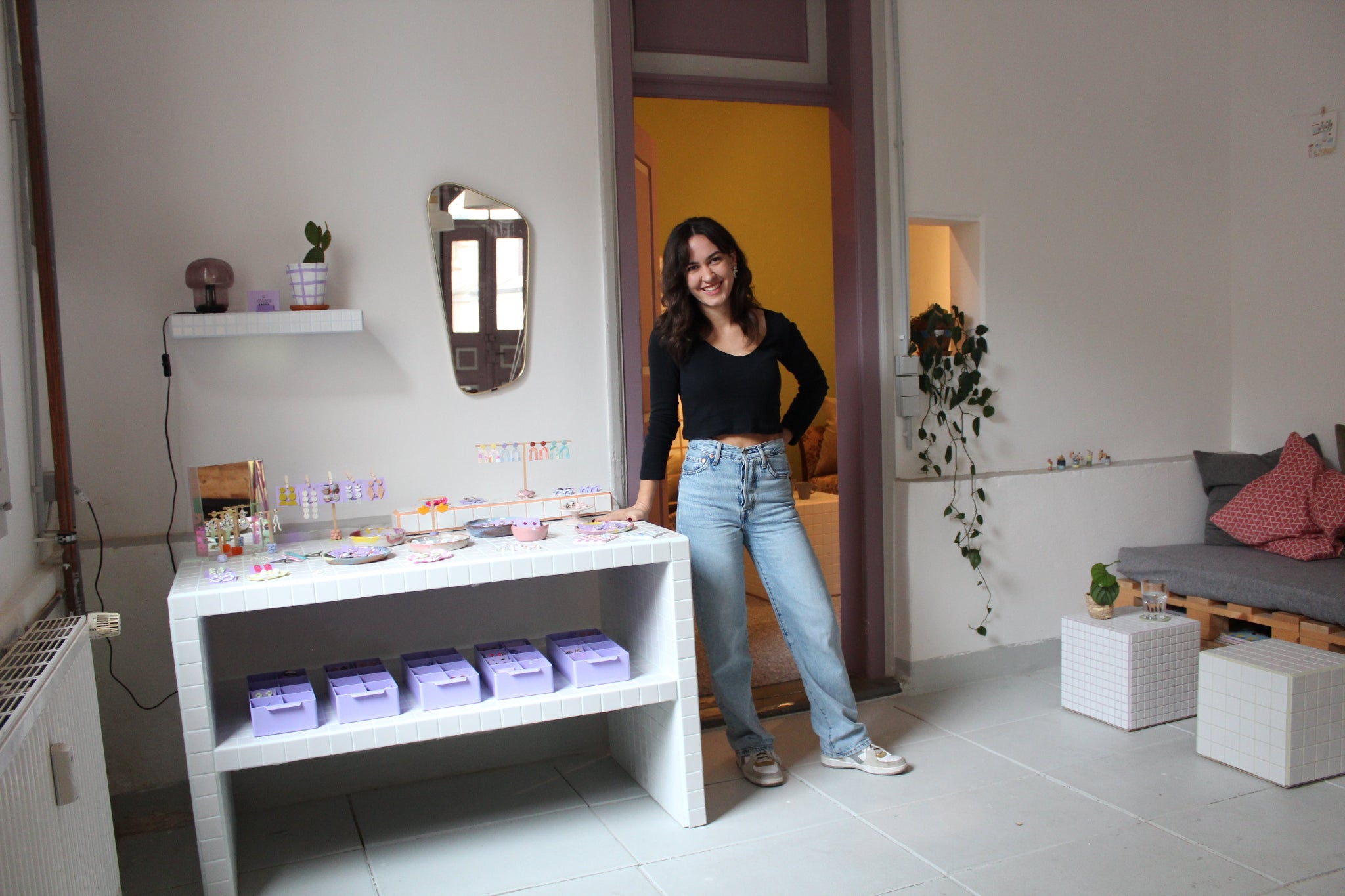 Schmuckdesignerin Alexandra Schütz steht neben einer Präsentationsfläche mit handgefertigtem Schmuck aus Polymerton in ihrem Atelier.