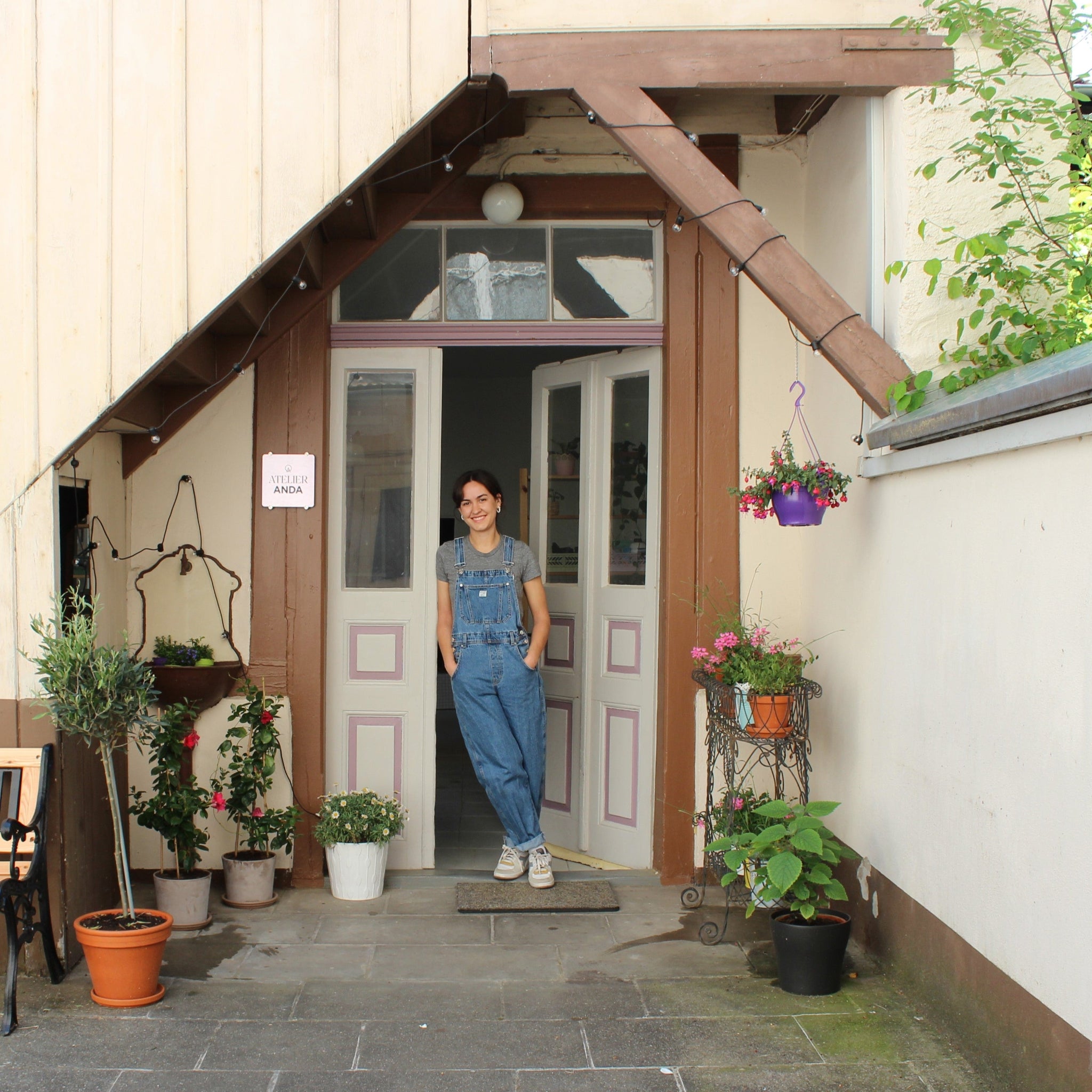 Schmuckdesignerin Alexandra Schütz steht im Eingang ihres Ateliers Anda, umgeben von Pflanzen und dem Außenbereich ihres Studios.