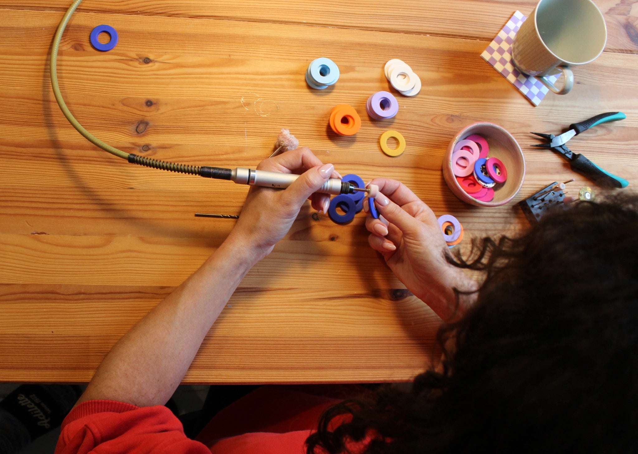 Schmuckdesignerin Alexandra Schütz schleift farbige Polymerton-Elemente mit einem Dremel an ihrem Werktisch, umgeben von Werkzeugen und vorbereiteten Schmuckteilen.