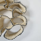 Detailansicht einer keramischen Wandskulptur mit offenem, durchbrochenem Aufbau, angelehnt an eine Korallenform; sandfarbene Oberfläche mit unregelmäßig geschwungenen Formen, entlang der Kanten mit rhythmisch gesetzten, schwarzen Pinselstrichen akzentuiert.
