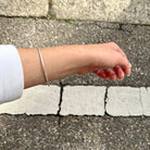 Silberner Armreif mit Haargummistruktur und Bördelung an der Schliesse, minimalistisch und handgefertigt, getragen an einem Handgelenk mit weissem Pulli.