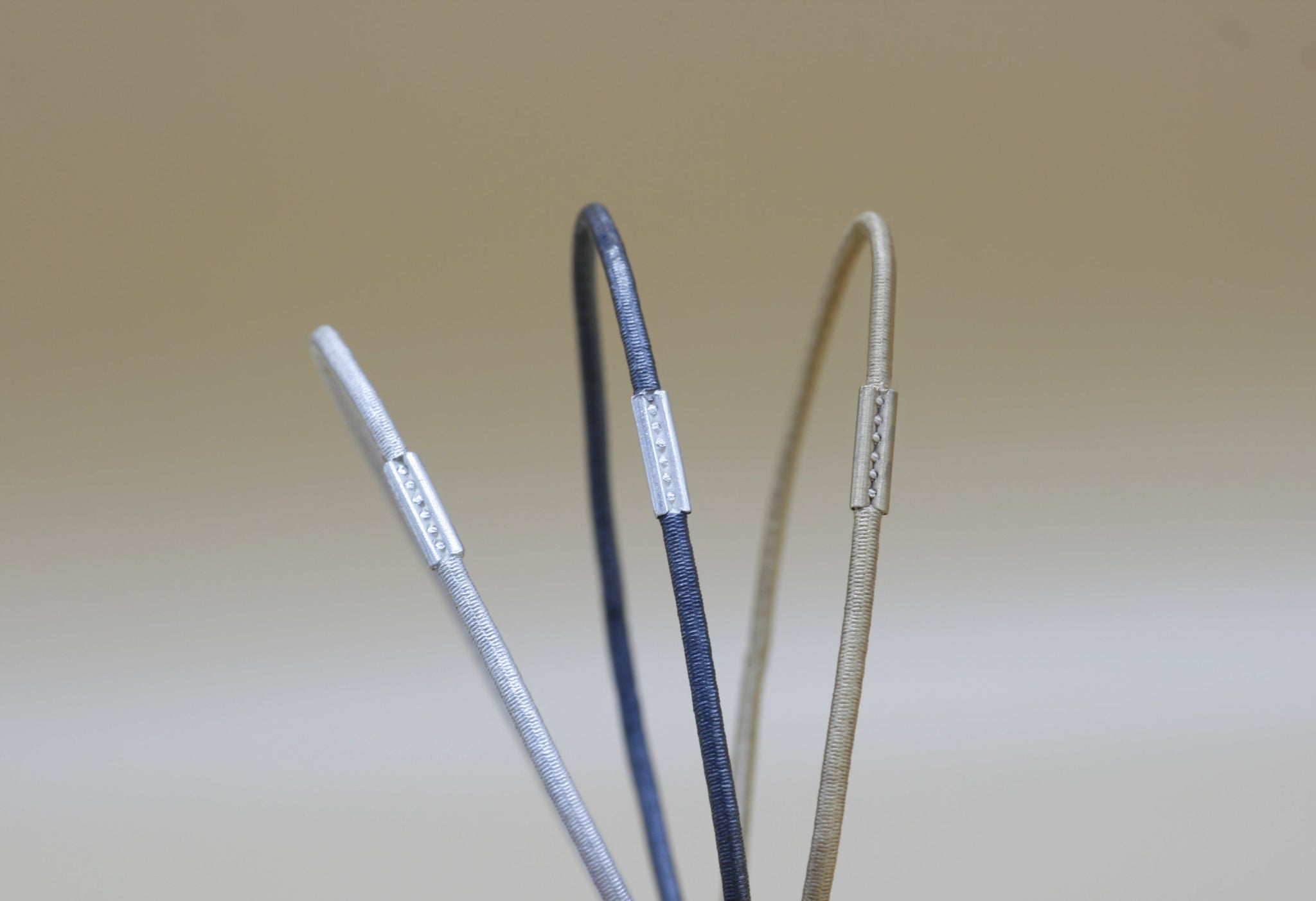 Drei Armreife aus Silber, Gold und Eisen, die von der Strassburger Künstlerin Annie Sibert so geschmiedet sind, dass sie aussehen wie Haargummis. 